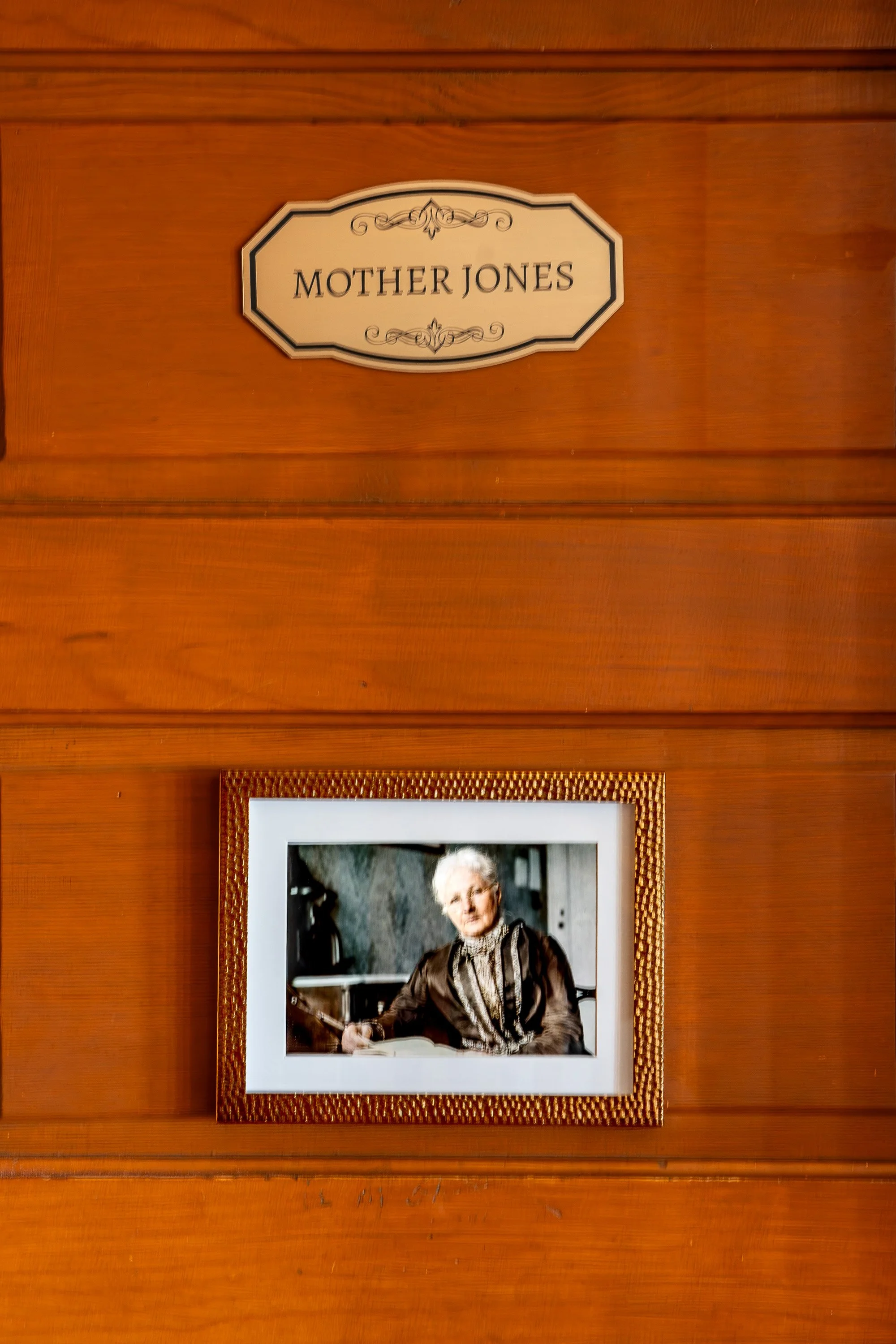 Close-up of a wooden framed photograph of an elderly woman holding a guitar, hanging on a wooden wall with a Mother's Day plaque above.