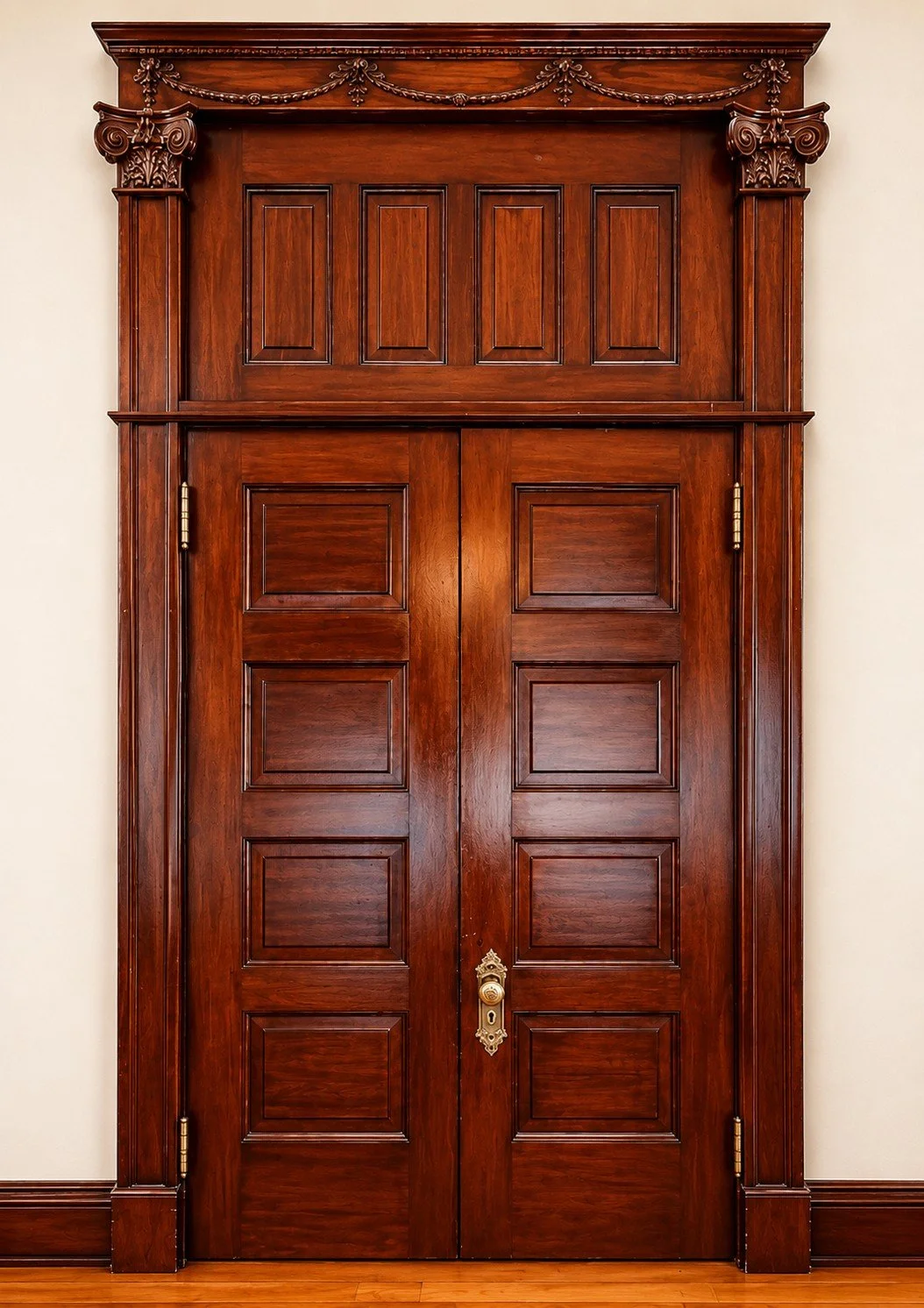 A large, ornate wooden double door with decorative molding and carved details. The door has a brass handle and hinges, with a light-colored wall on each side.