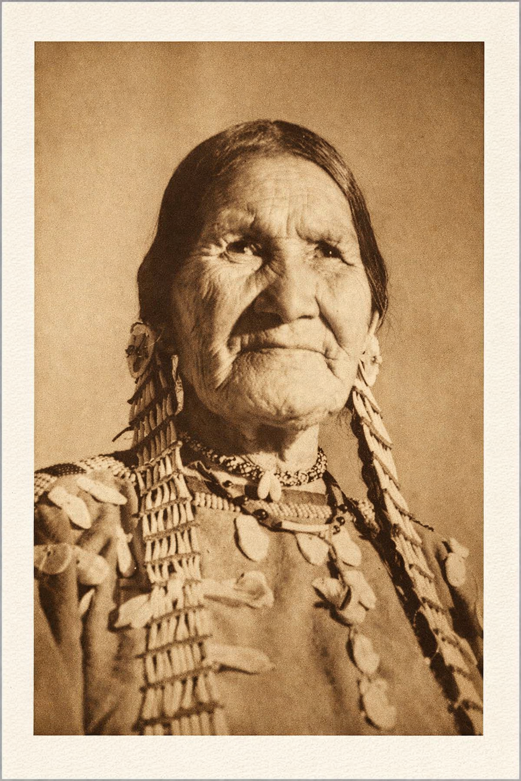 Sepia-toned portrait of an elderly Native American woman with traditional jewelry and clothing.