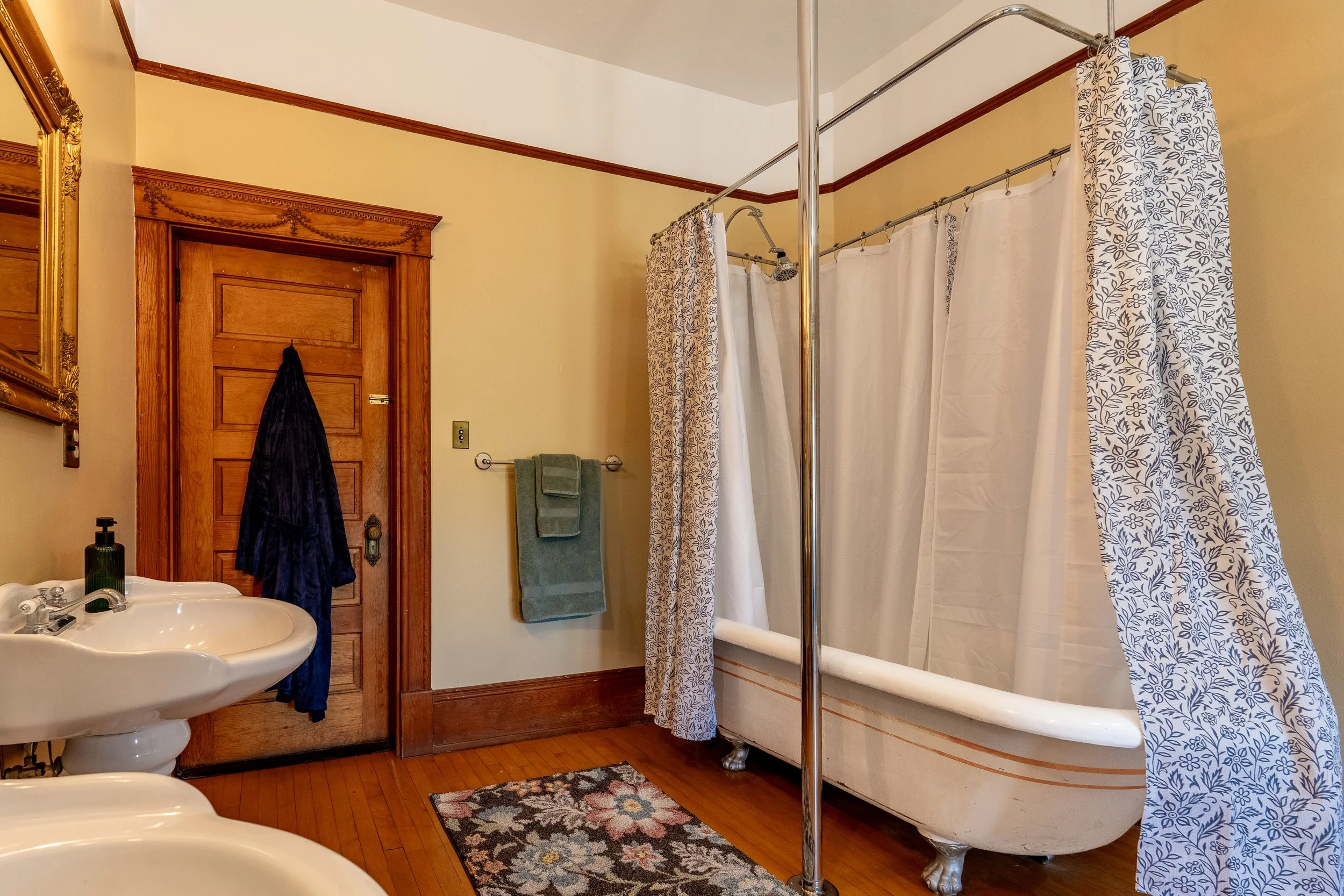 A bathroom with a vintage clawfoot bathtub, shower curtain, sink, and wooden door with trim.