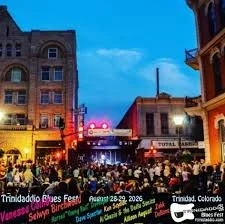 Crowd gathered at downtown street festival in Trinidad, Colorado, at night with colorful lights and historic buildings.