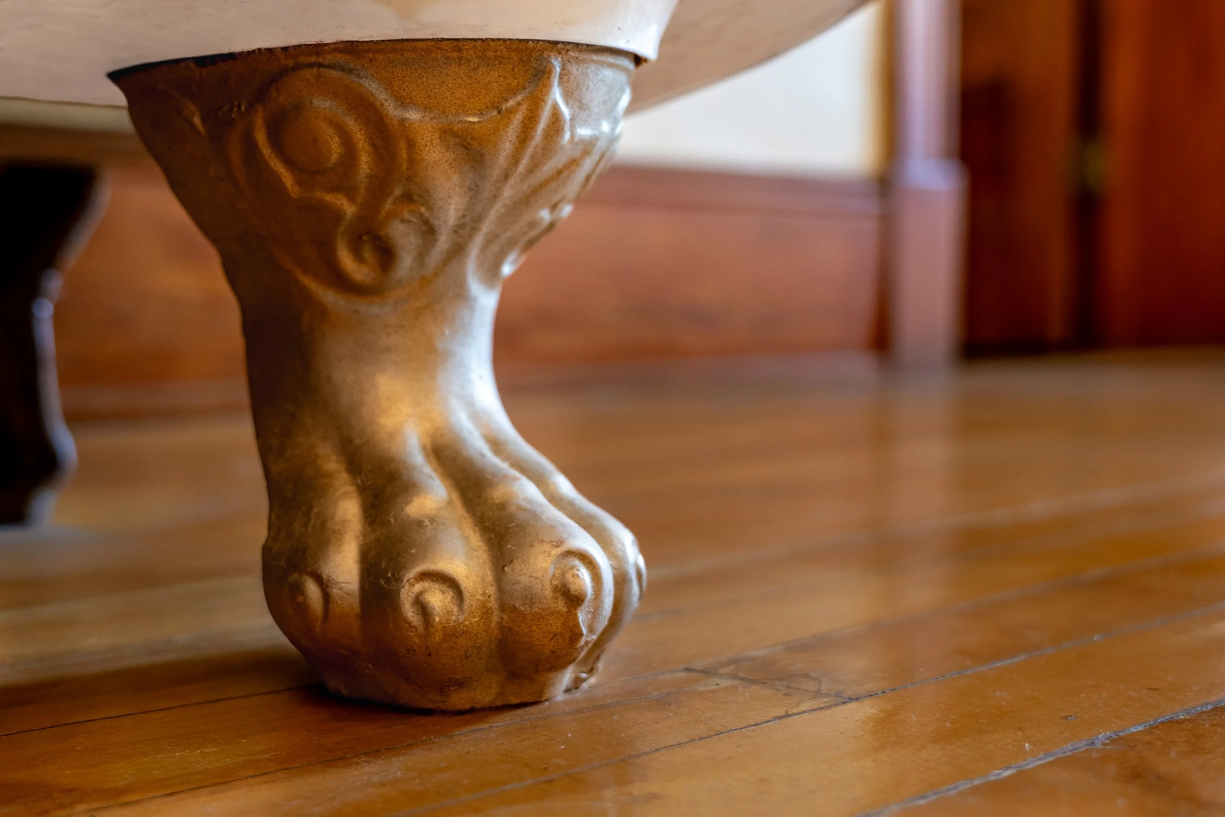 Close-up of a carved wooden furniture leg with intricate swirling designs, resting on a hardwood floor.