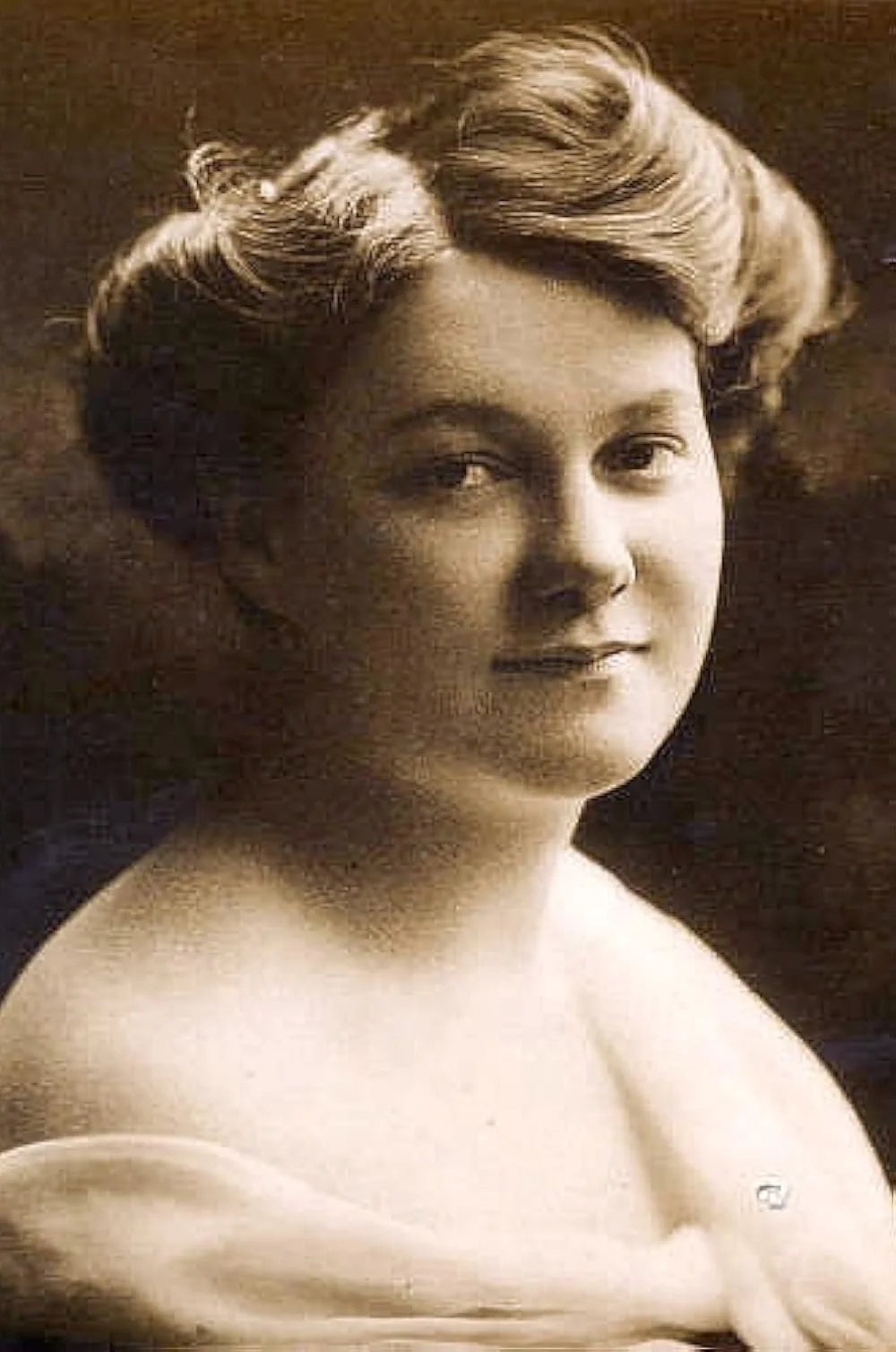 Sepia portrait of a woman with short, wavy hair, smiling slightly, with shoulders exposed.