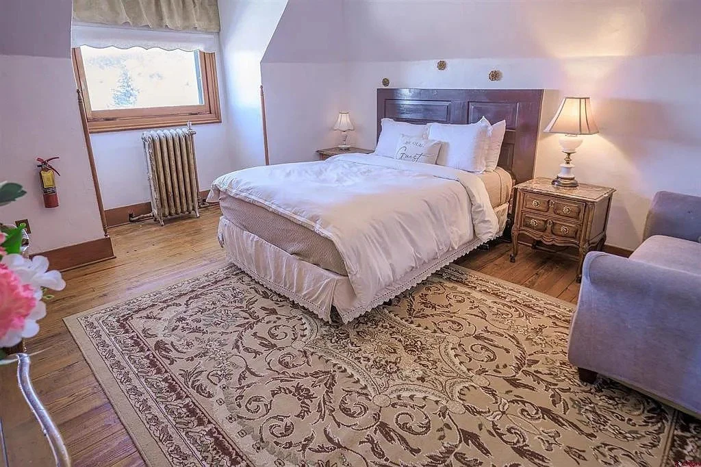 A cozy bedroom with a large bed, nightstand with lamp, armchair, and window with curtains.