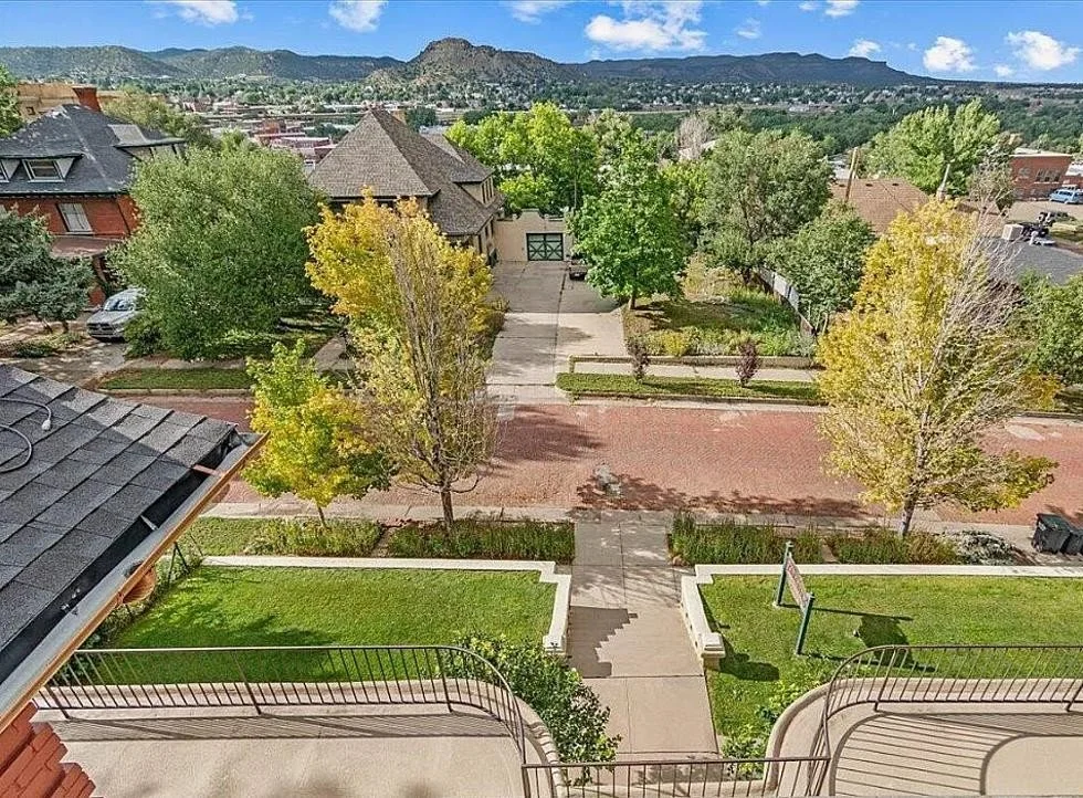 A view from a balcony looking down on a residential neighborhood with trees, a brick street, and a mountain range in the background.