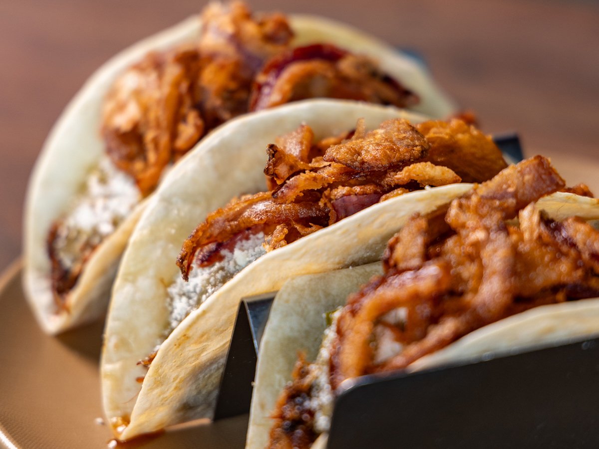 Three tacos filled with seasoned meat and toppings, served in soft corn tortillas.
