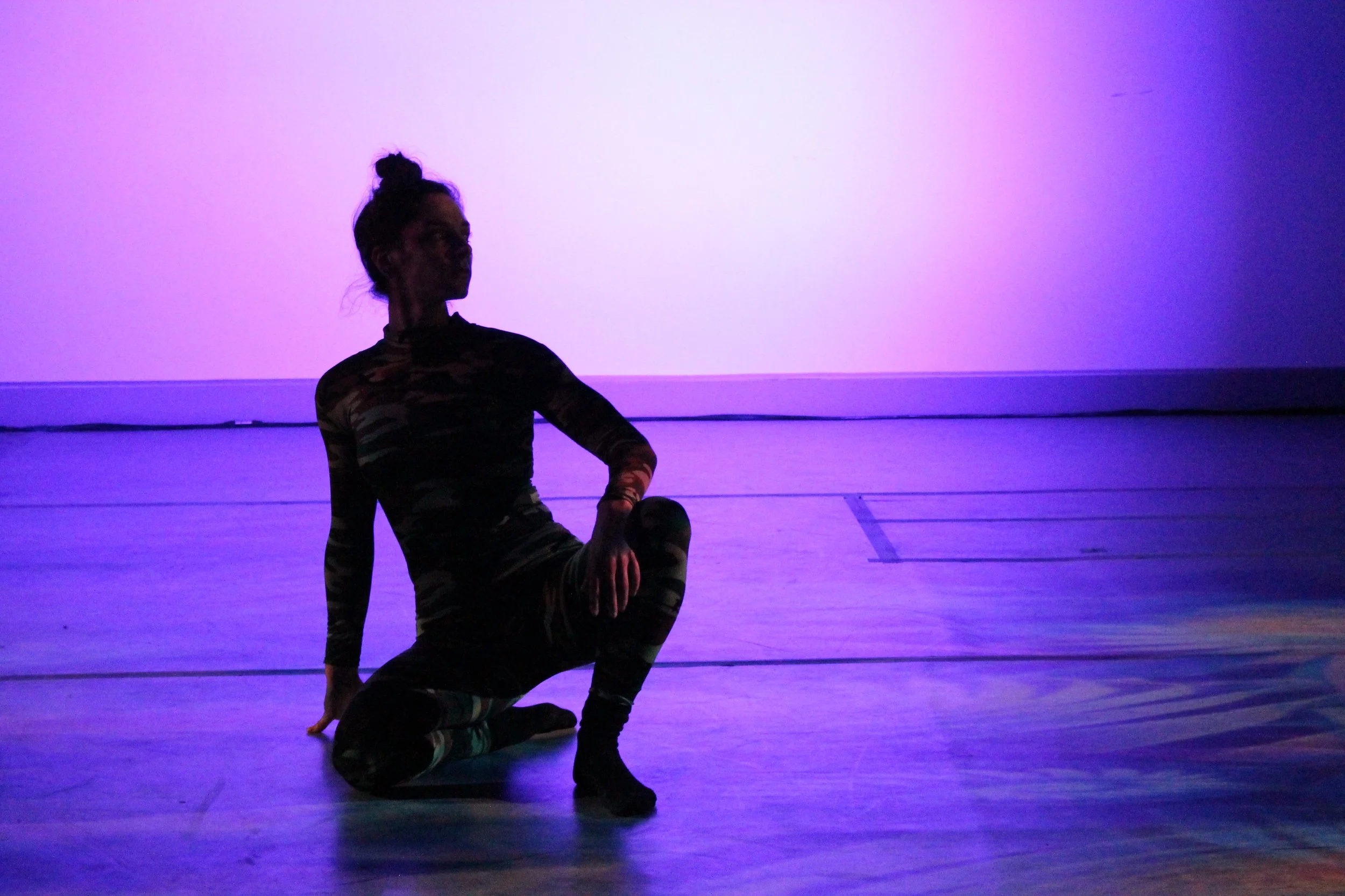 Anna sits onstage, lit in silhouette. Lighting is pink and purple.