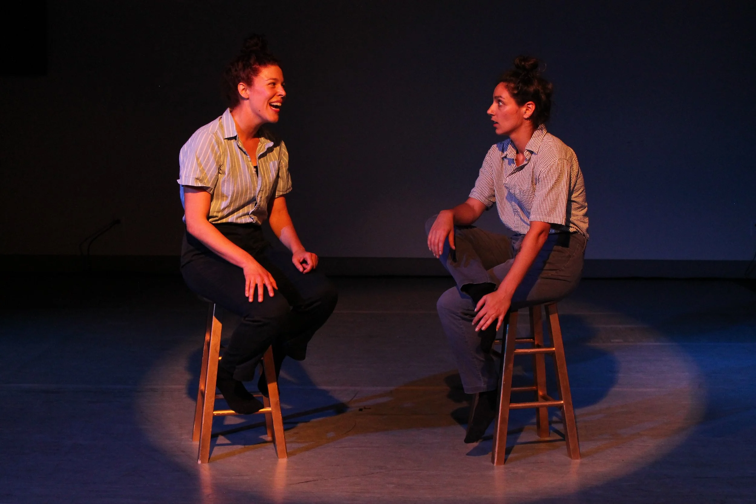 Leah and Anna have a conversation. They sit on stools. 