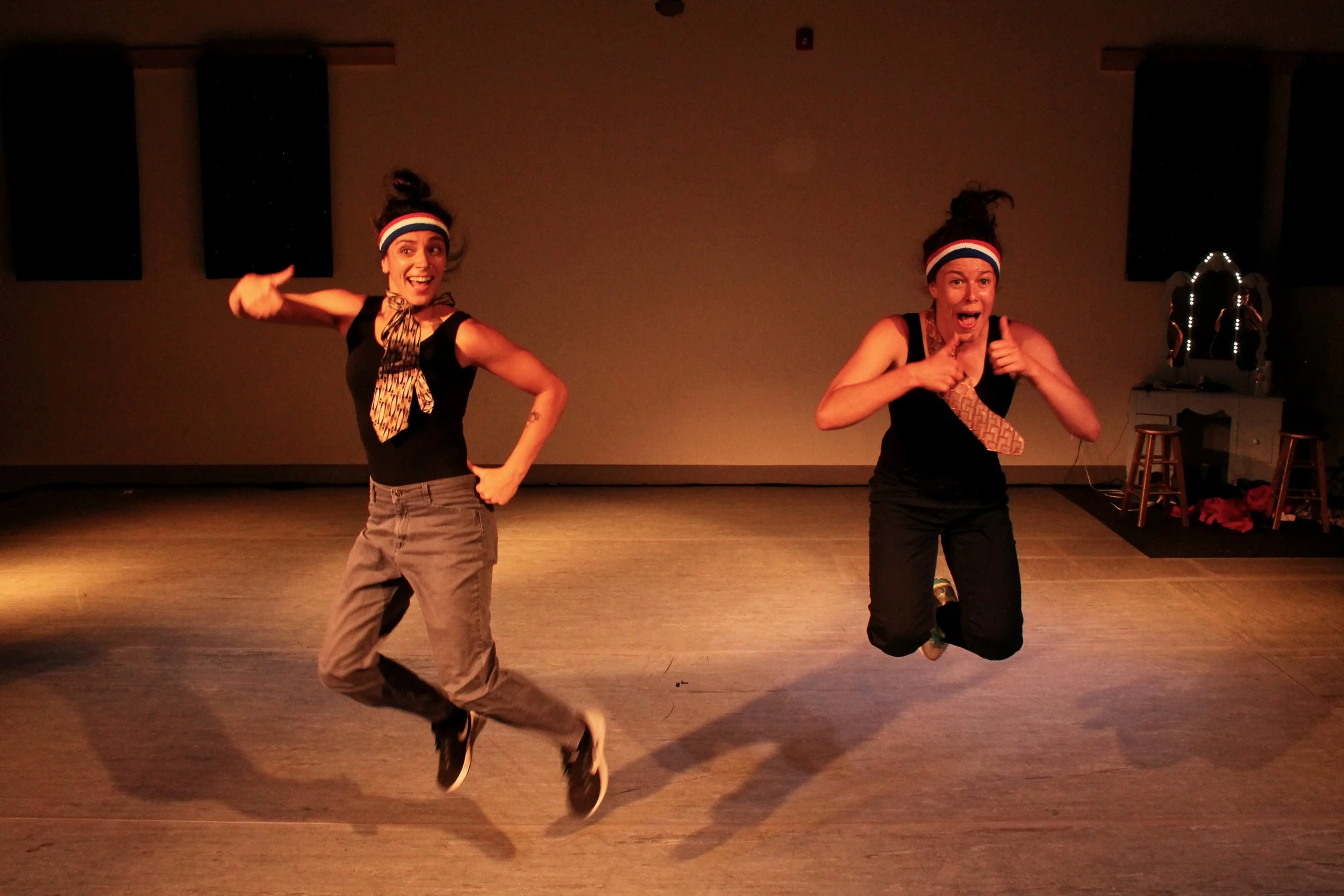 Leah and Anna wear workout gear. They jump and give enthusiastic thumbs up to the audience.