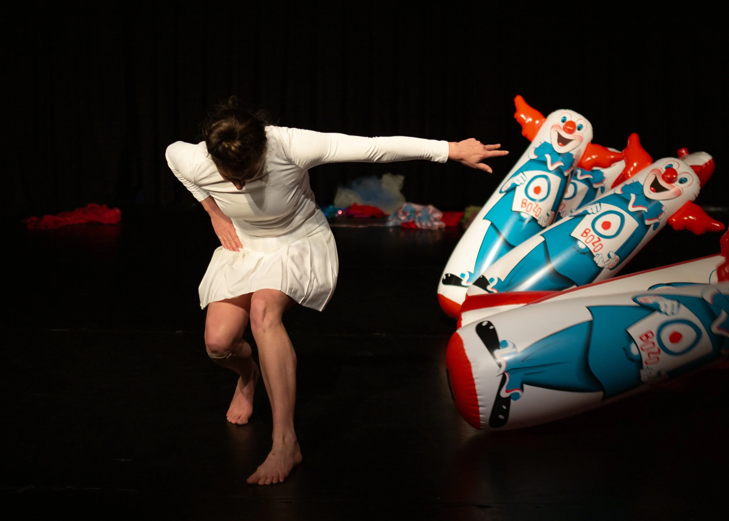 Anna bends forward with one arm outstretched. She knocks down a row of inflatable Bozo dolls.
