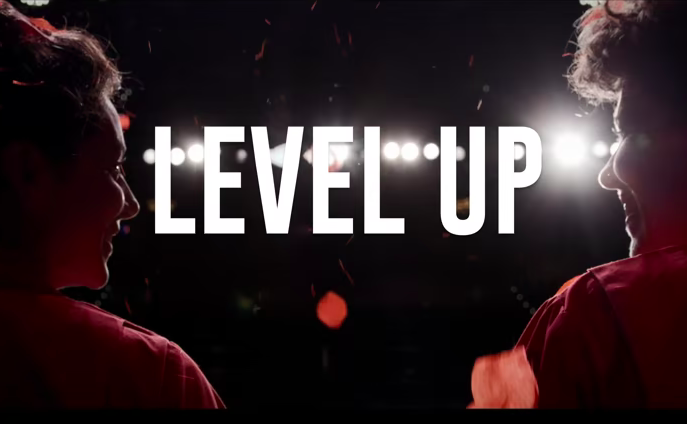 Anna and Leah can be seen from behind, looking out at bright stage lights. The words LEVEL UP are in white in the center of the image.