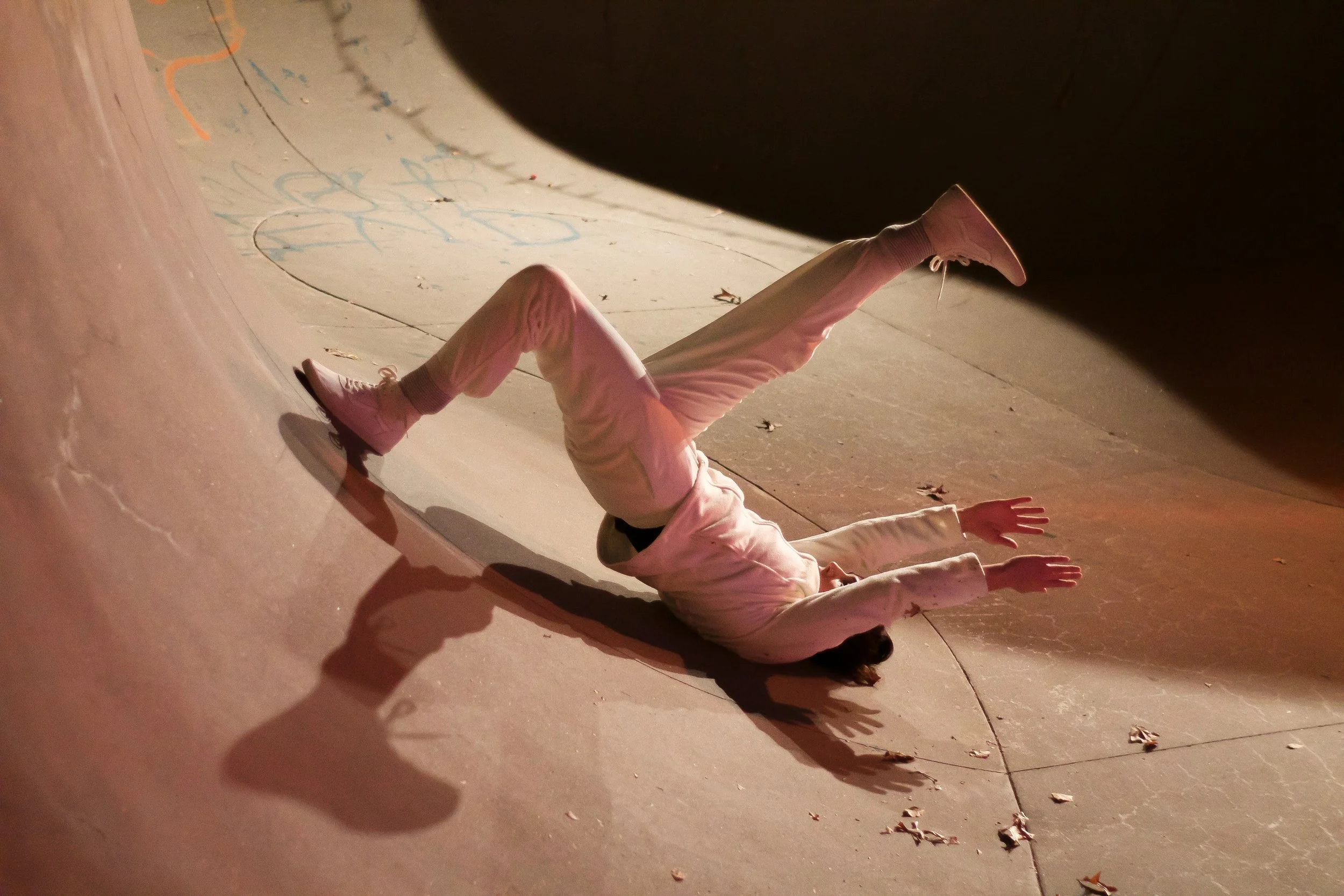 Anna wears all white. She lies on her back in a one legged bridge position with both arms stretched overhead.