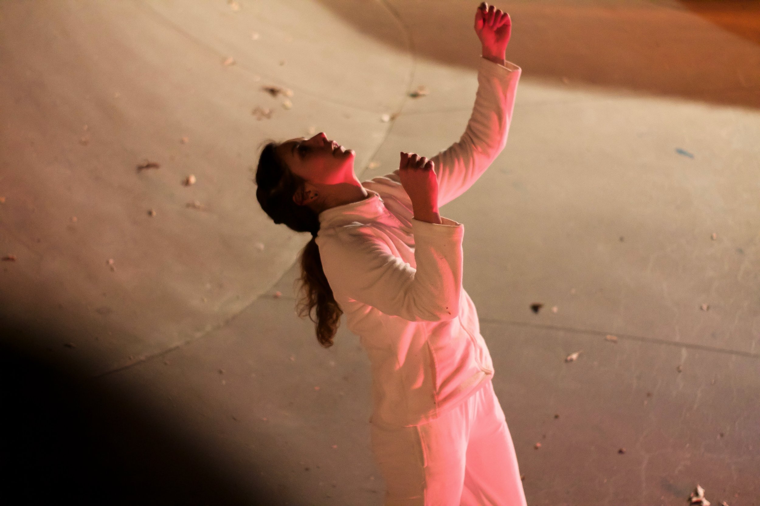 Anna wears all white. She gestures upwards. She is in a bowl at the skate park.