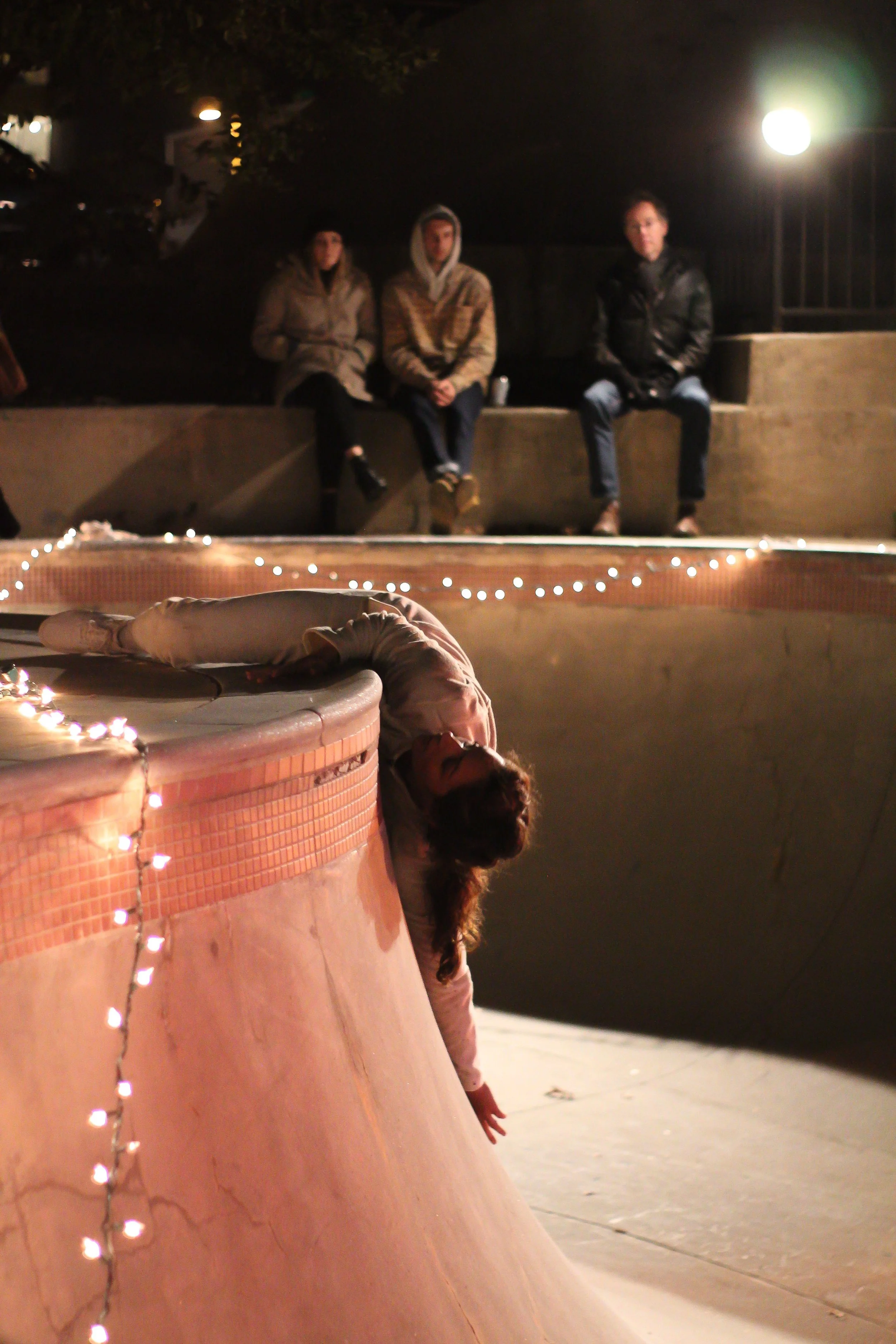 Anna wears all white. She drapes her body halfway over the ledge of the bowl at the skate park. Twinkle lights are hung along the edge. Audience members sit on the edge of the skate park, watching Anna dance.