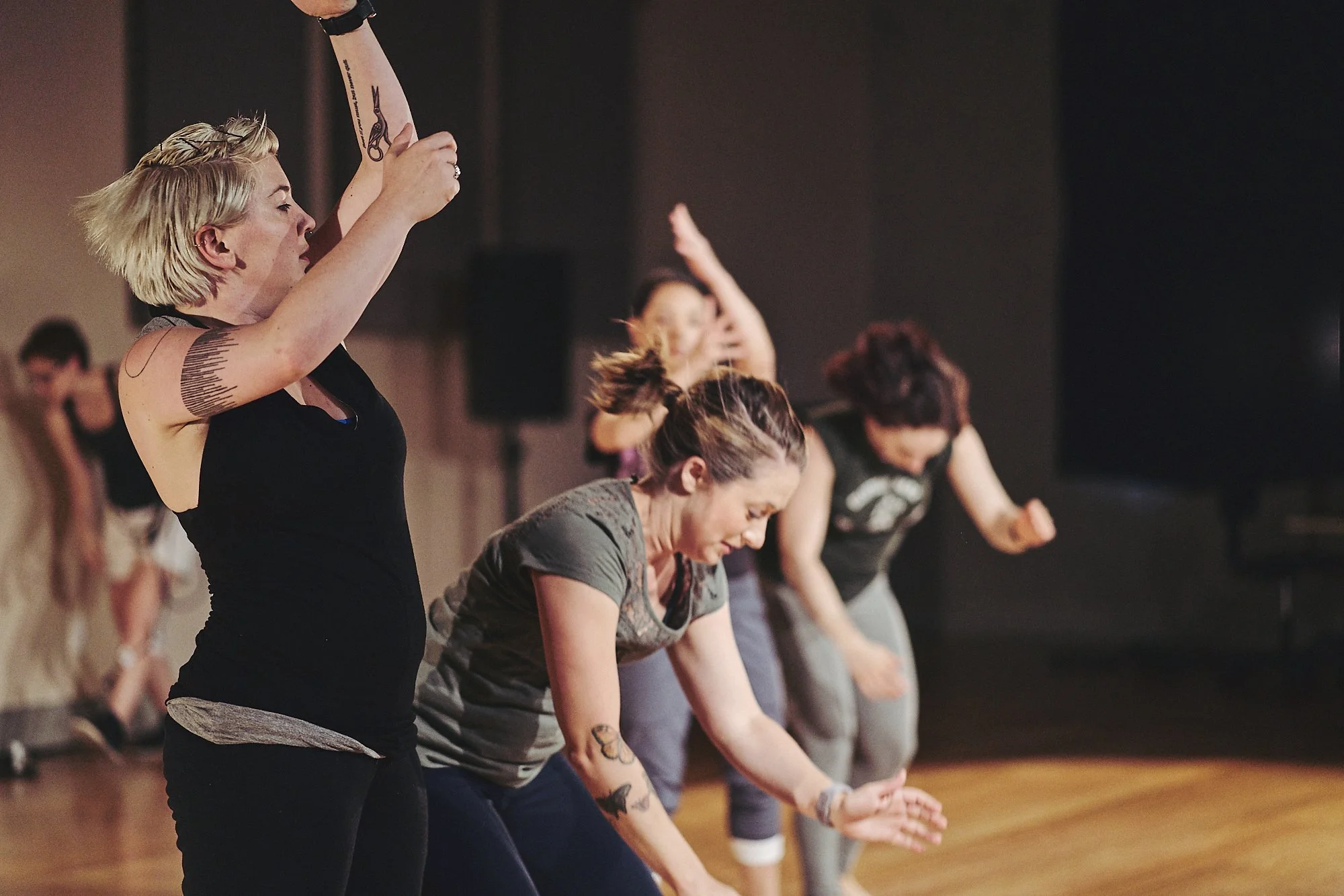 Four dancers in rehearsal clothes perform a gestural phrase near the front of the stage.