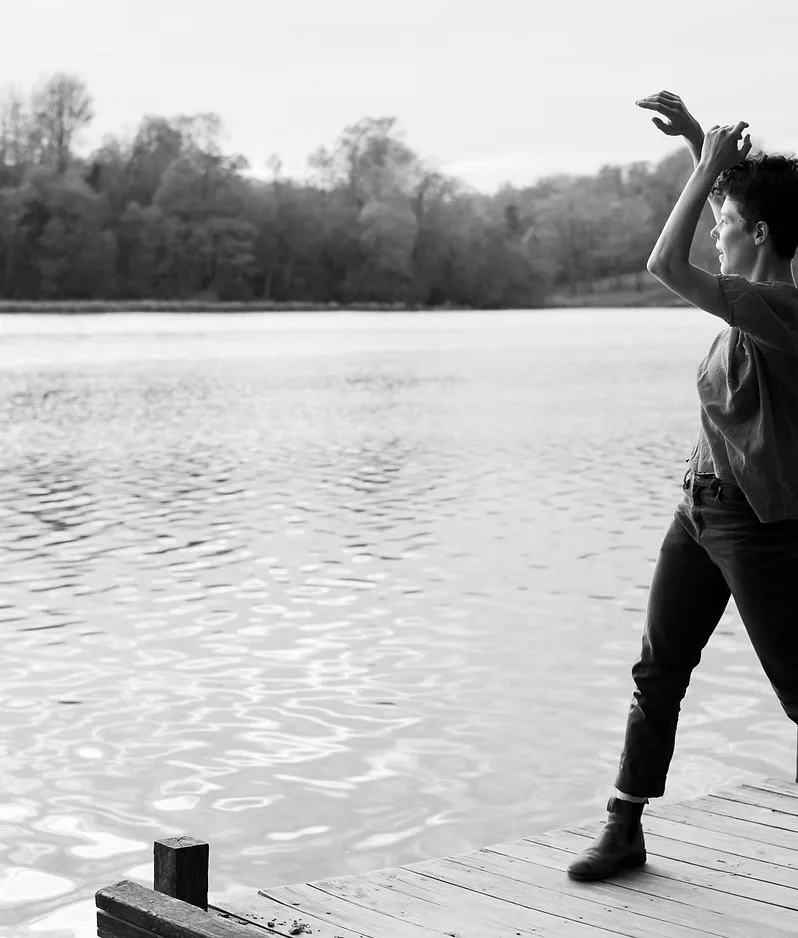 Leah dances near a lake. The photo is in black & white.