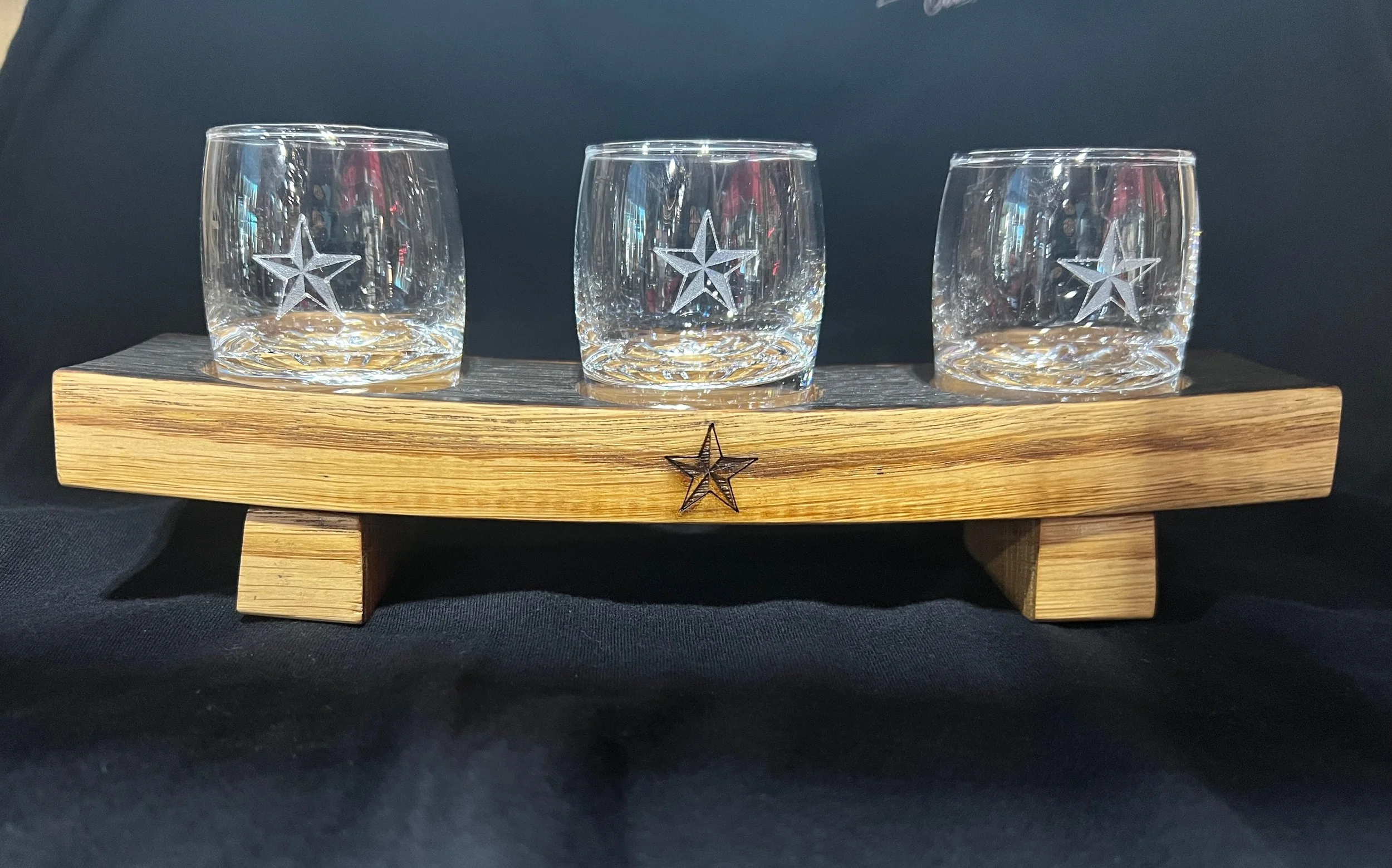 Three clear glass tumblers with star etchings, placed on a rectangular wooden tray with star decorations, against a black background.