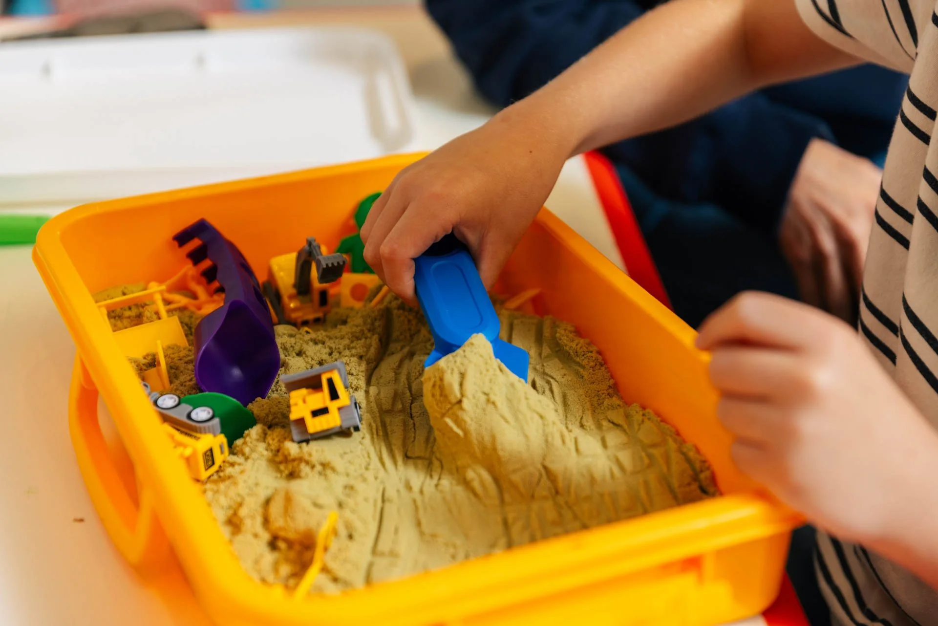 Child playing in a sandbox with toy construction vehicles and tools.