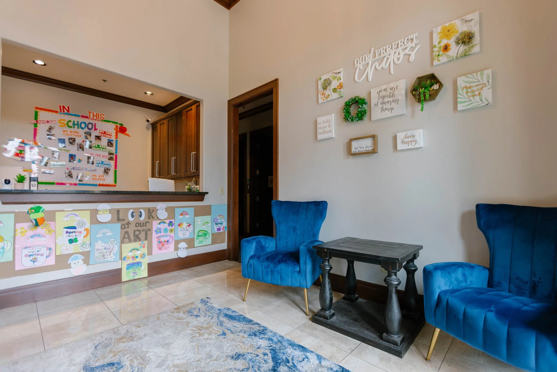 Interior of a living room with blue velvet chairs, a black side table, and wall decorations including framed quotes and artwork.