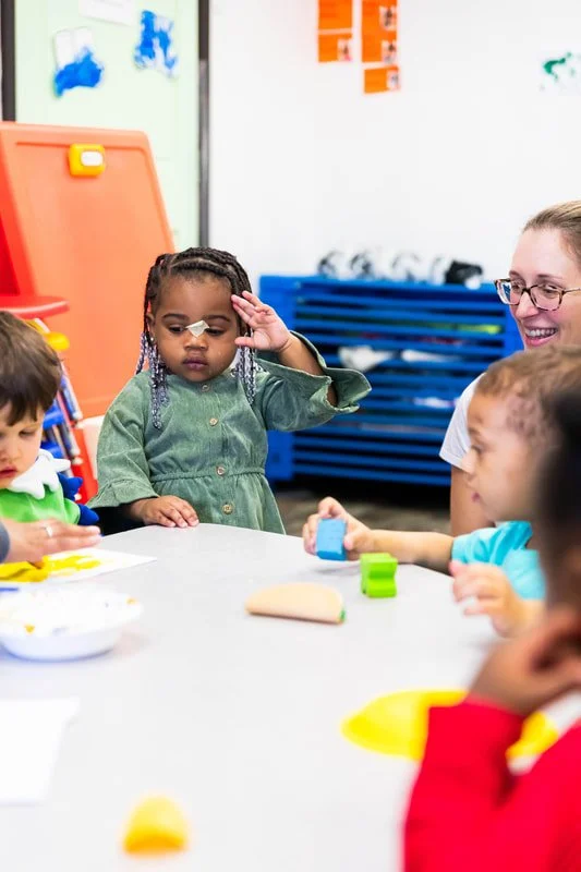 Children and a teacher in a classroom engaged in an activity at a table.