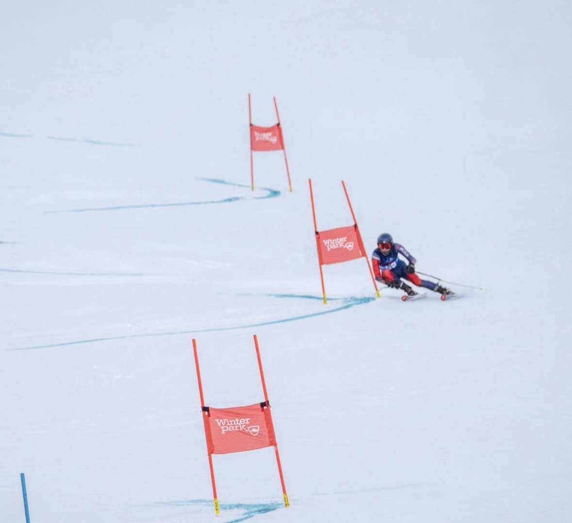 A skier in racing gear navigating through slalom gates on a snowy slope during a race.