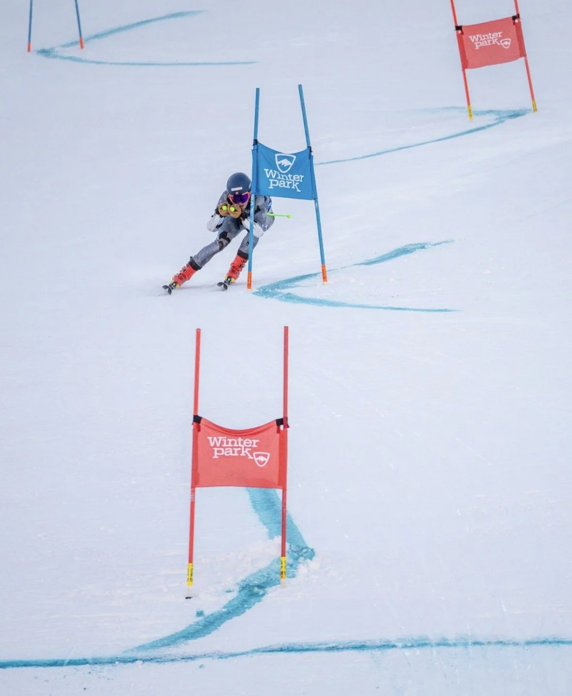 A young skier in black gear and a helmet navigates a slalom course marked with red and blue gates at Winter Park ski resort.