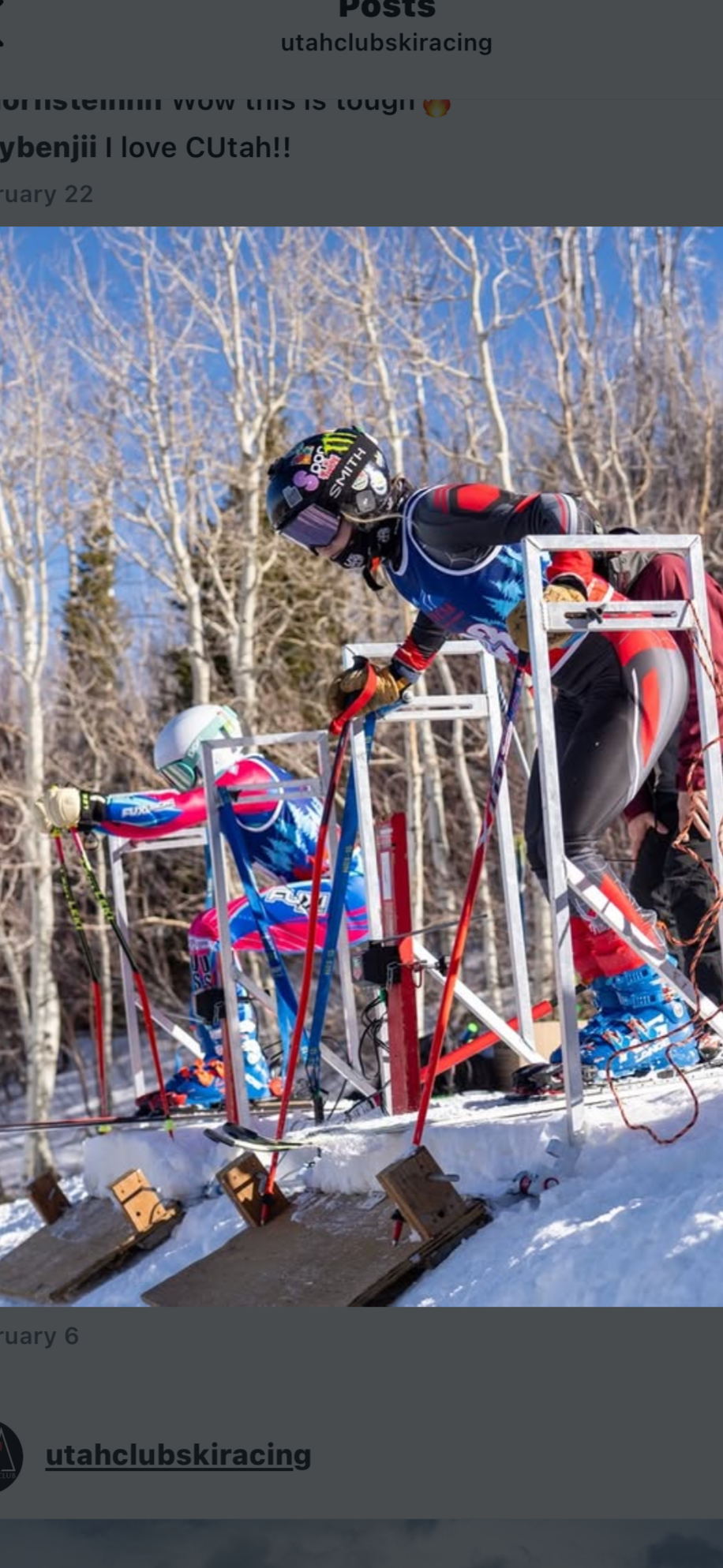 Cross-country skiers preparing at a snowy trail with a snow-covered forest and clear blue sky in the background.