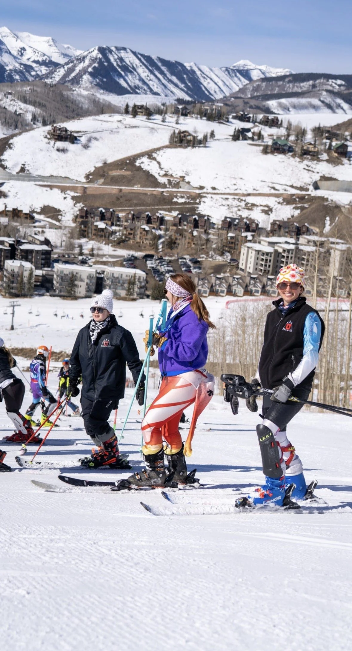 Group of people cross-country skiing on a snowy mountain landscape with ski gear and winter clothing, with houses and mountains in the background.