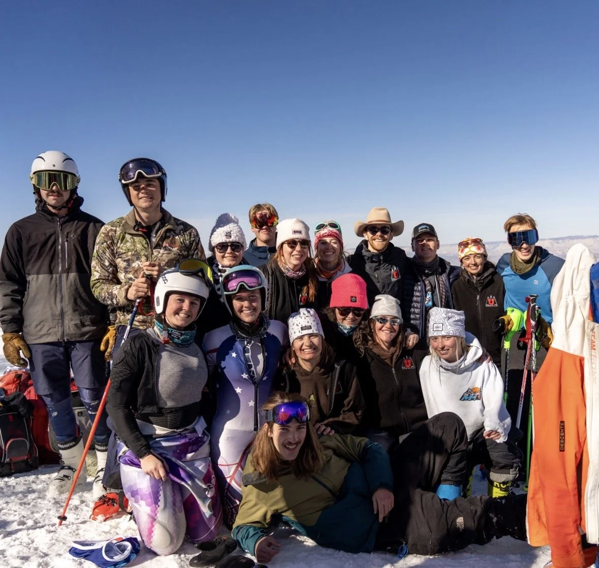 A group of people in ski gear posing together on a snowy mountain with a clear blue sky.