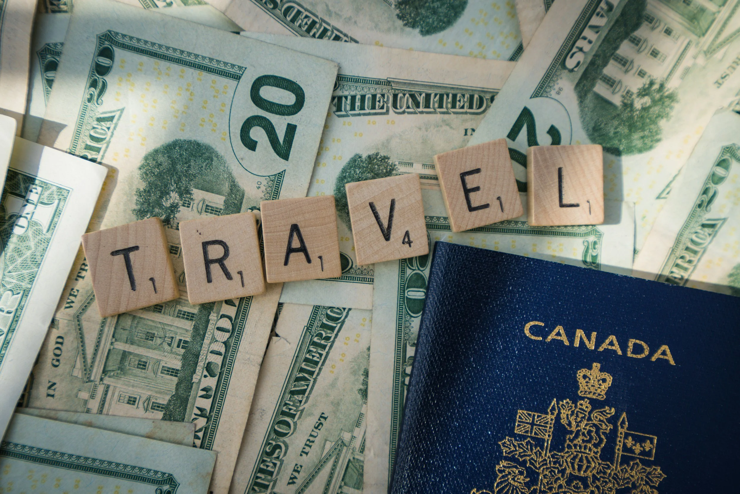 Various U.S. twenty-dollar bills, a Canadian passport, and Scrabble tiles spelling the word "TRAVEL".