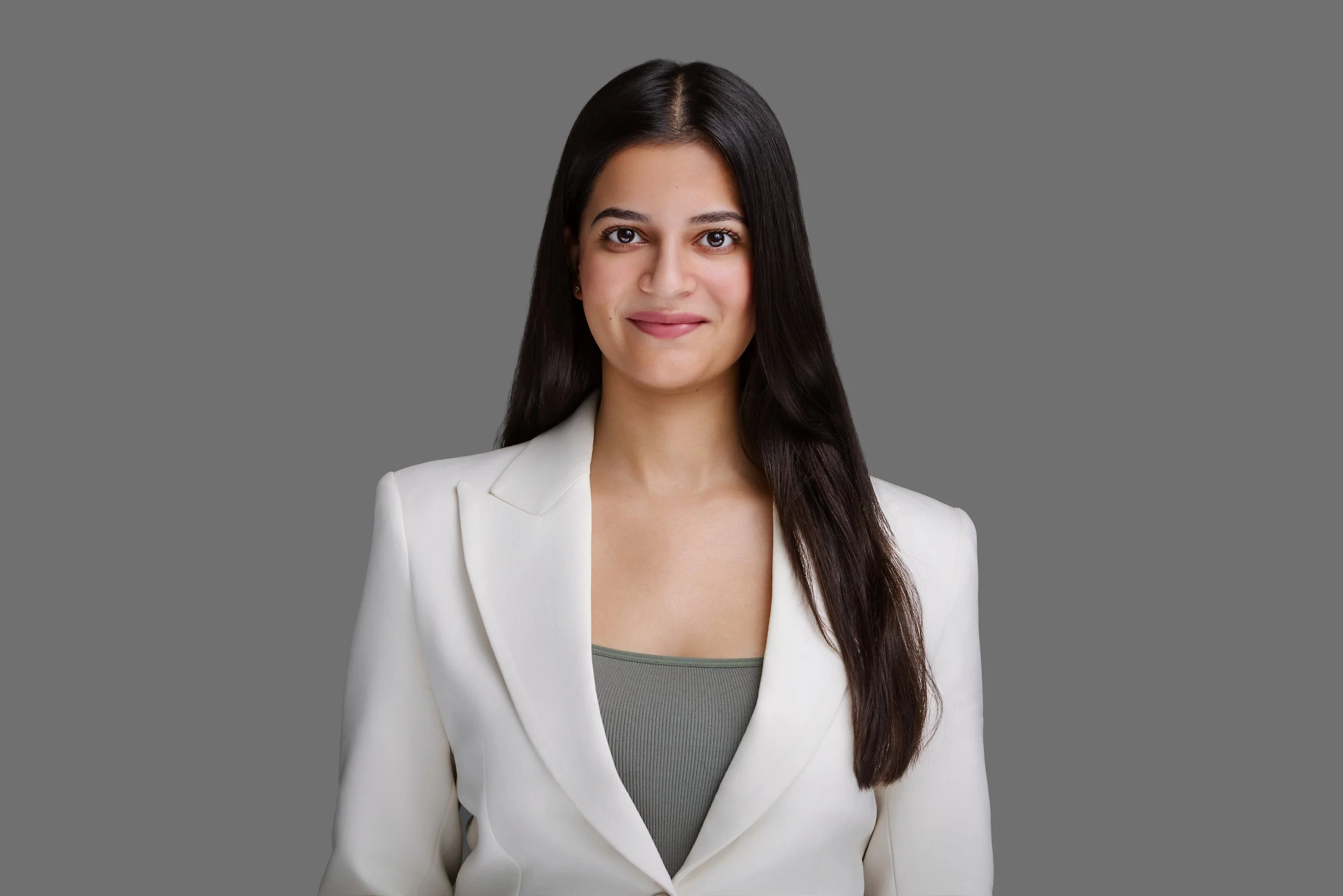 Portrait of a woman with long dark hair wearing a white blazer and gray top against a gray background.