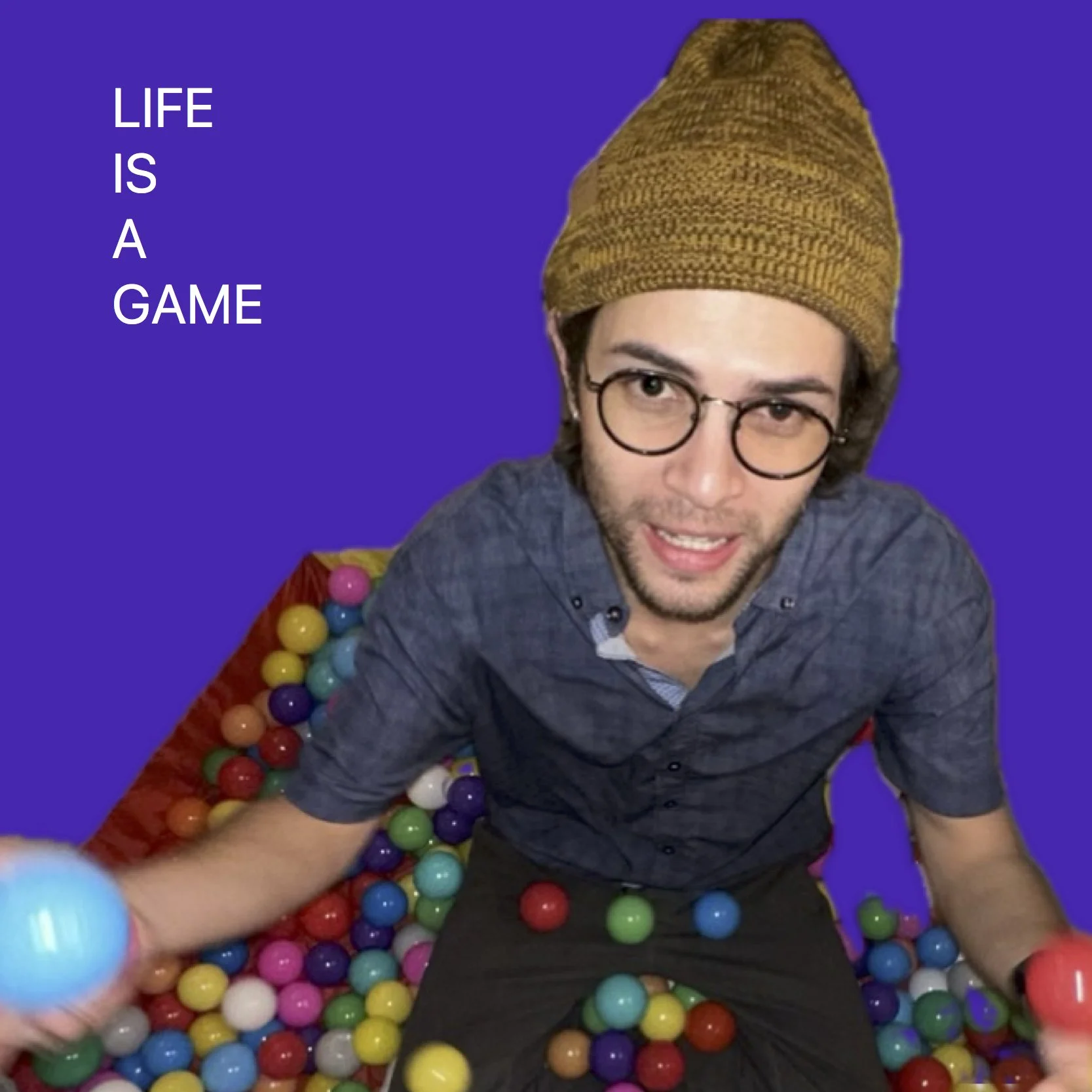 A man with glasses and a beanie smiling while sitting in a ball pit filled with colorful plastic balls. The background is purple and there is a quote on the left side that reads 'Life is a game'.