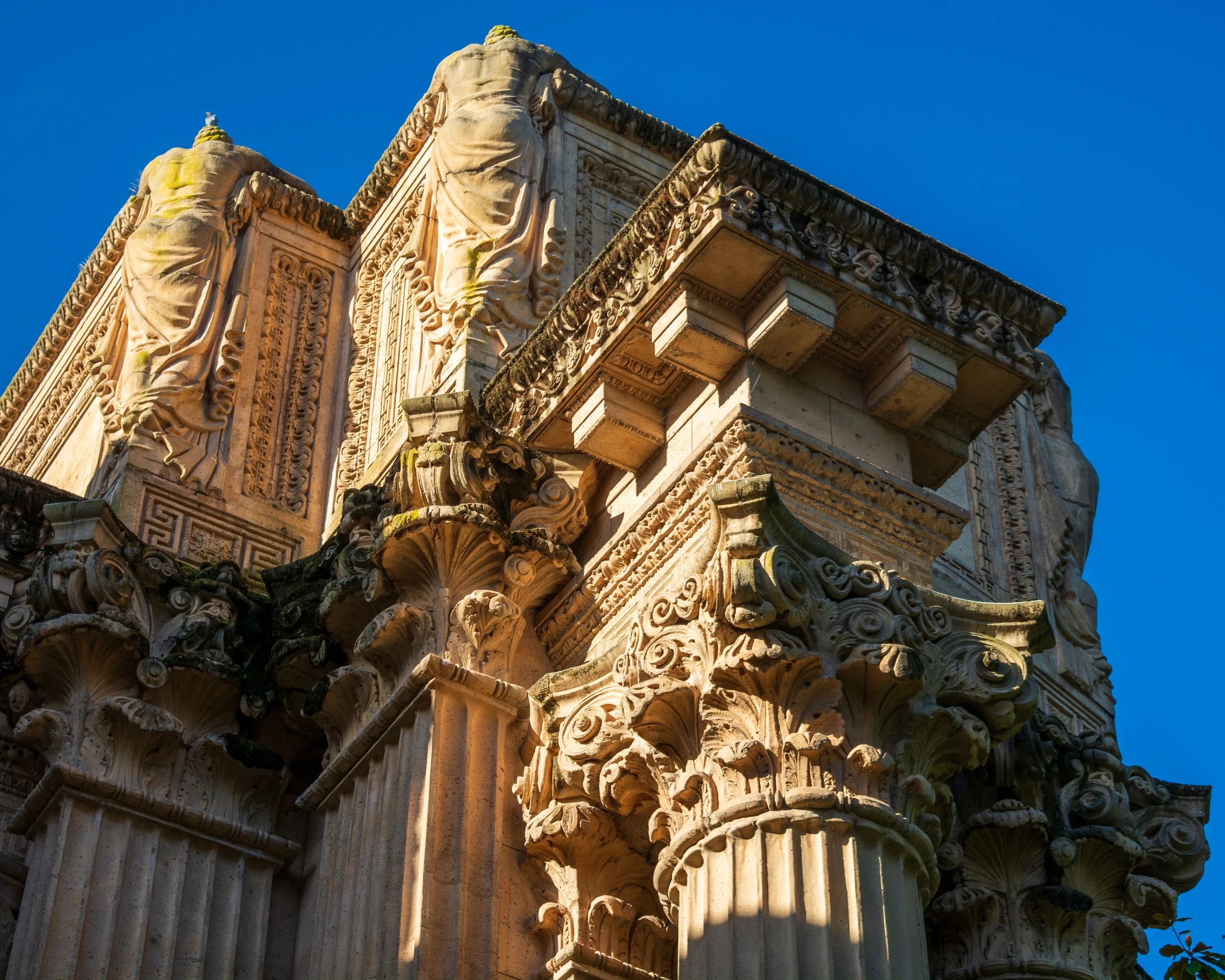 Close-up of the top section of an elaborately decorated ancient stone column with detailed carvings and a scalloped design, set against a clear blue sky.