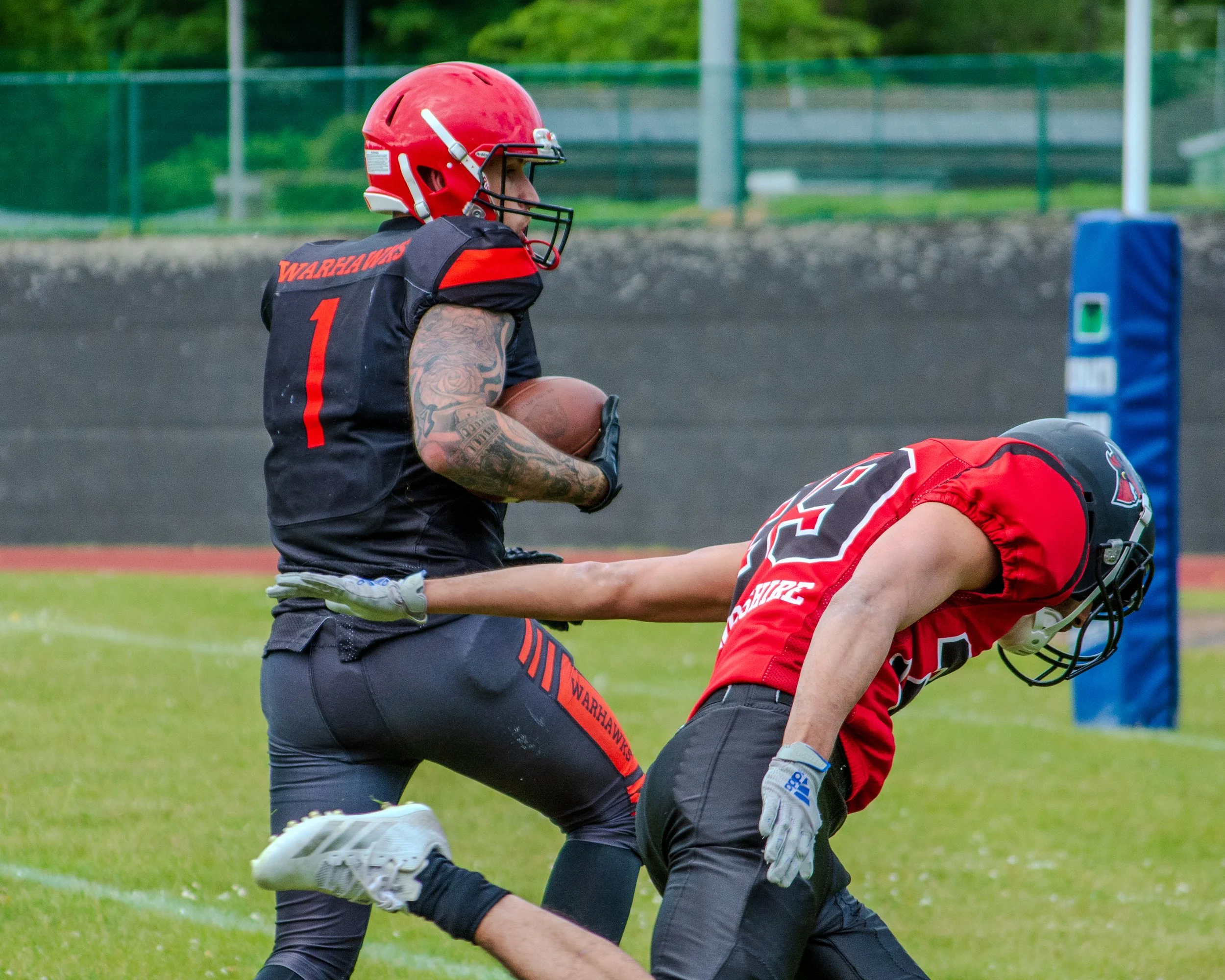 A football player in a black and red uniform with a red helmet holding a football on a field during a game.