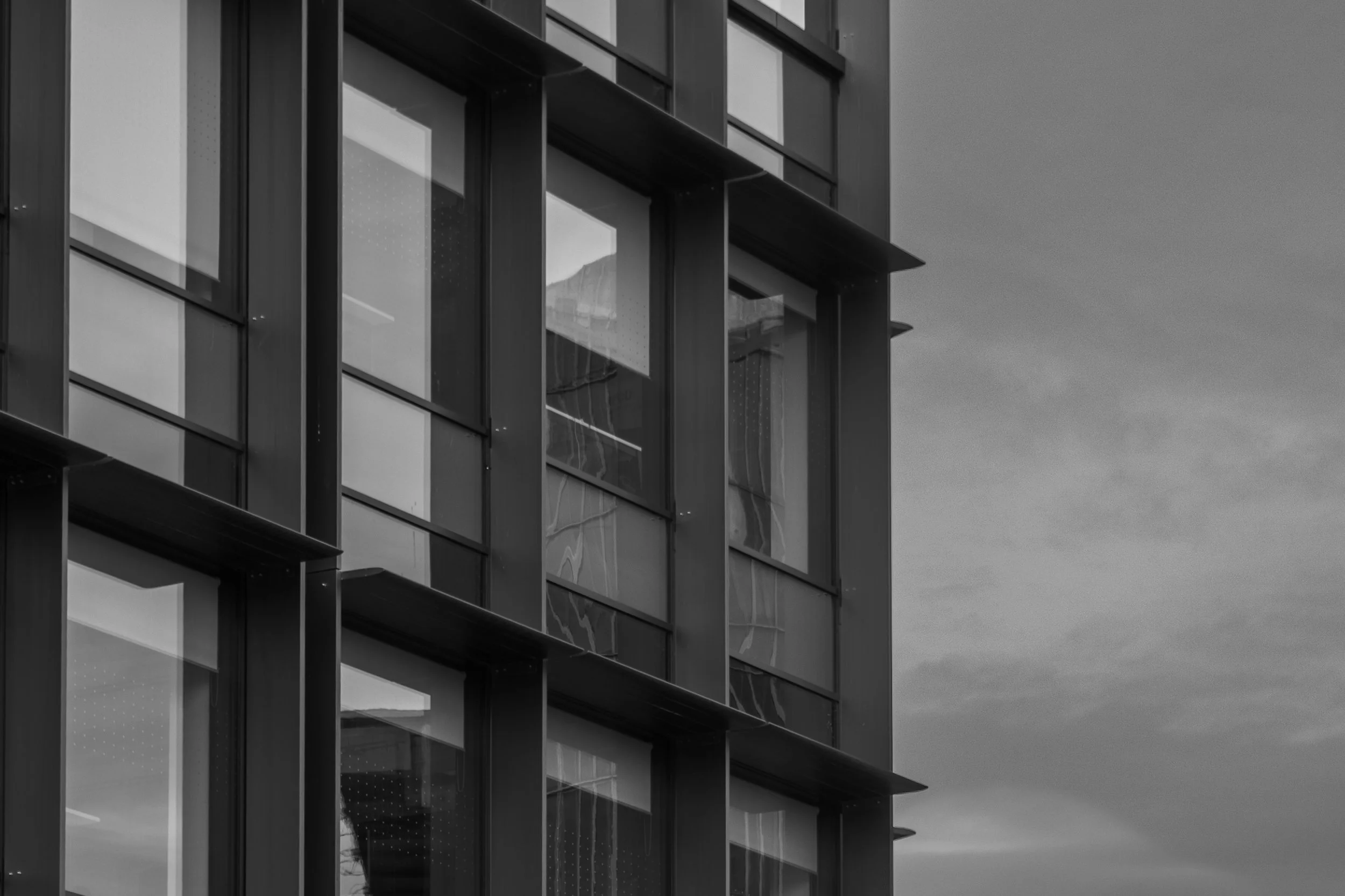 Close-up view of a modern building with multiple glass windows and exterior structure, black and white photo.
