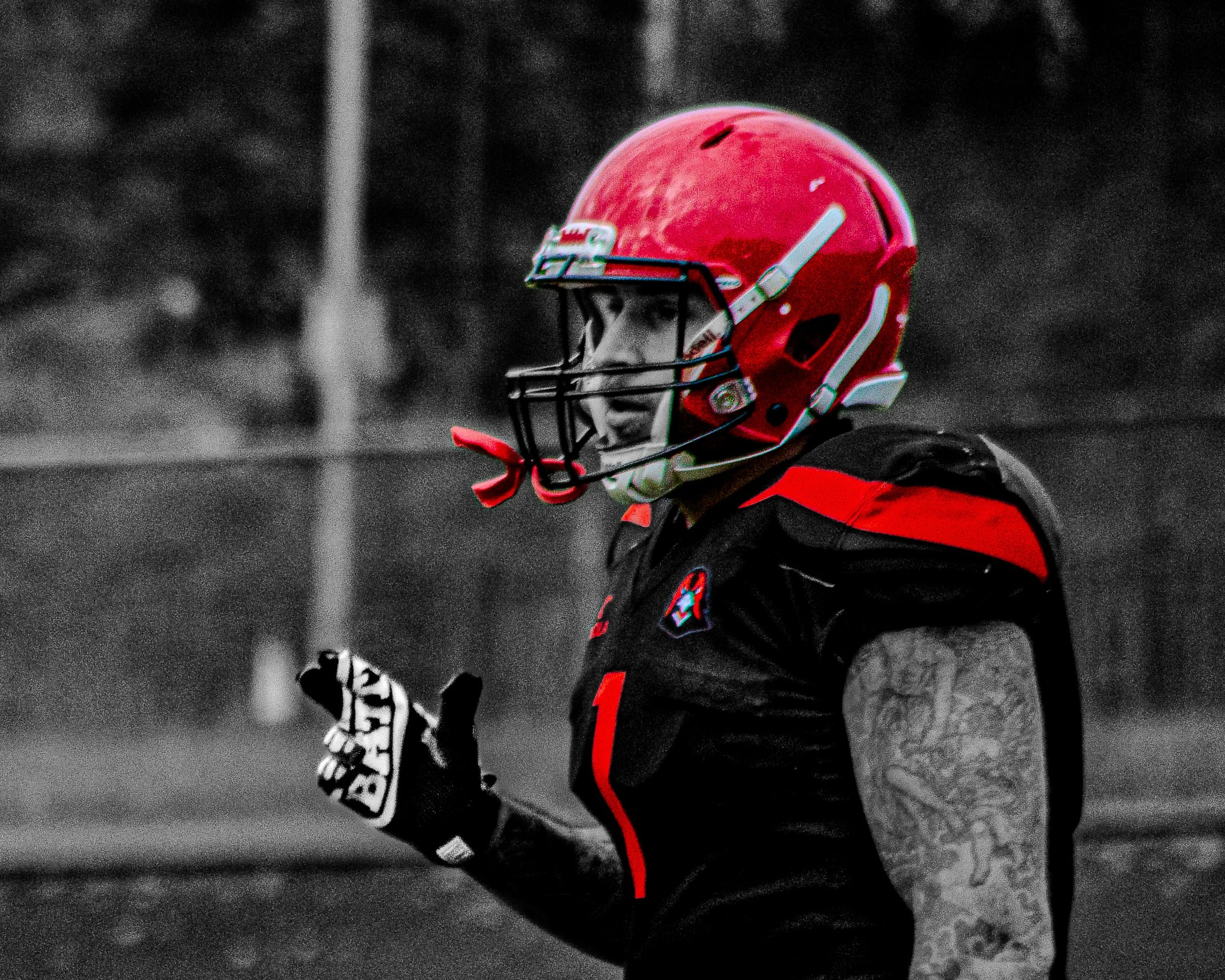 Close-up of a football player wearing a red helmet and black uniform, with a game field in the background.
