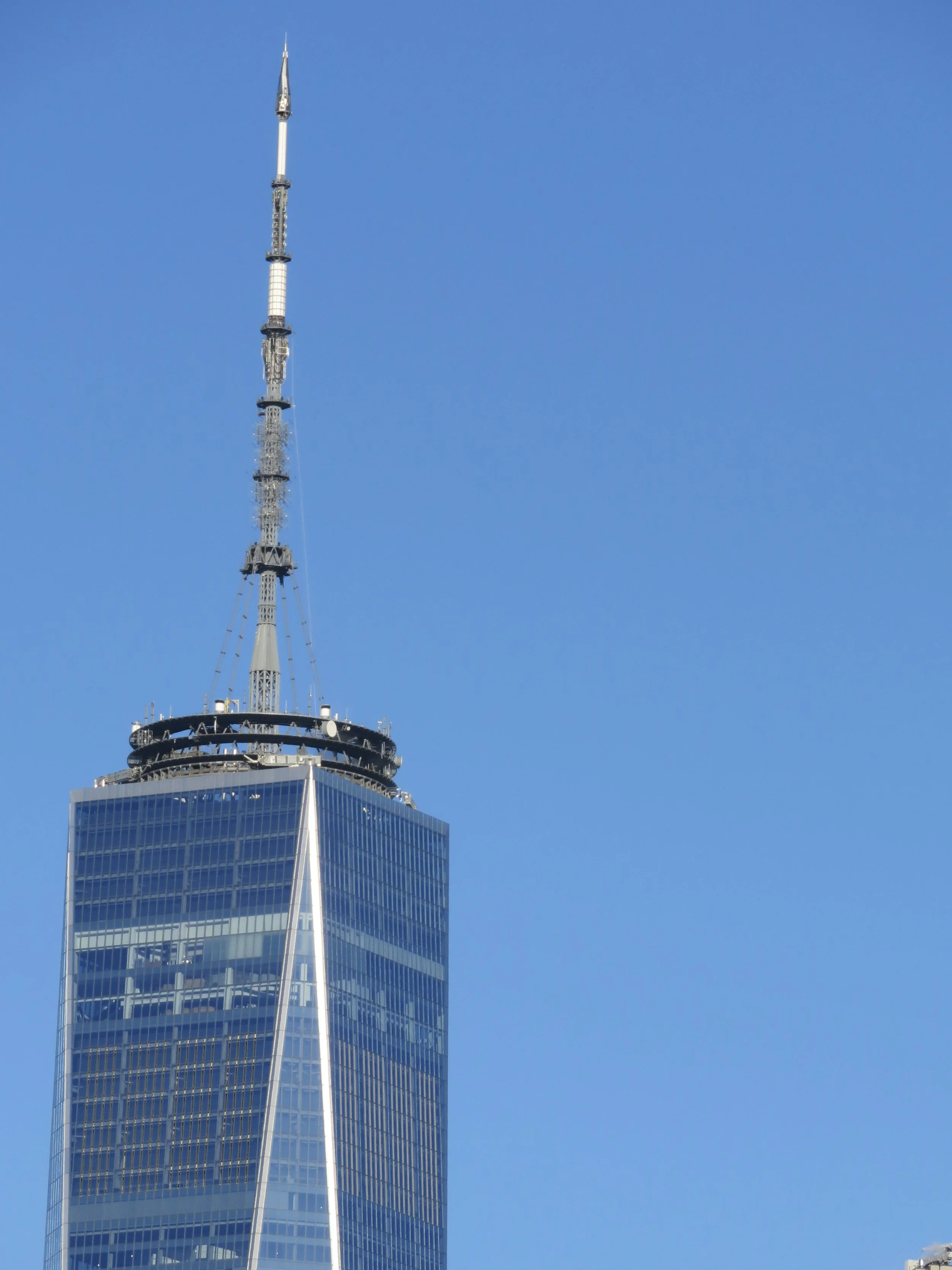 The One World Trade Center building with its pointed spire, reflecting sunlight, against a clear blue sky.