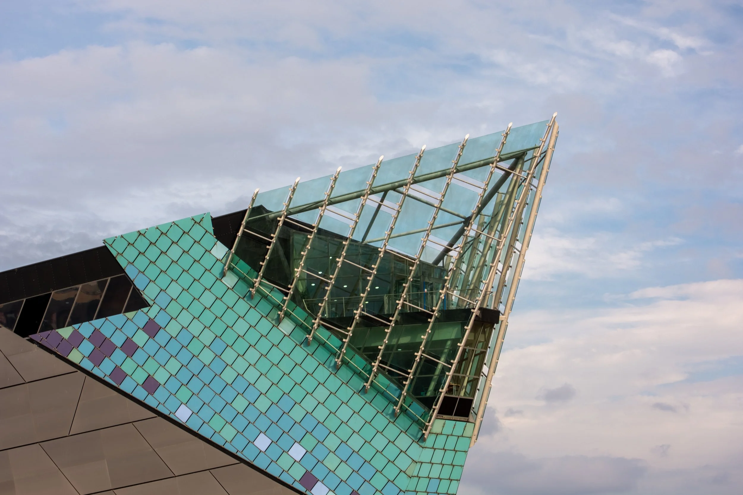 Modern building with colorful iridescent glass panels and architectural fins, against a partly cloudy sky.