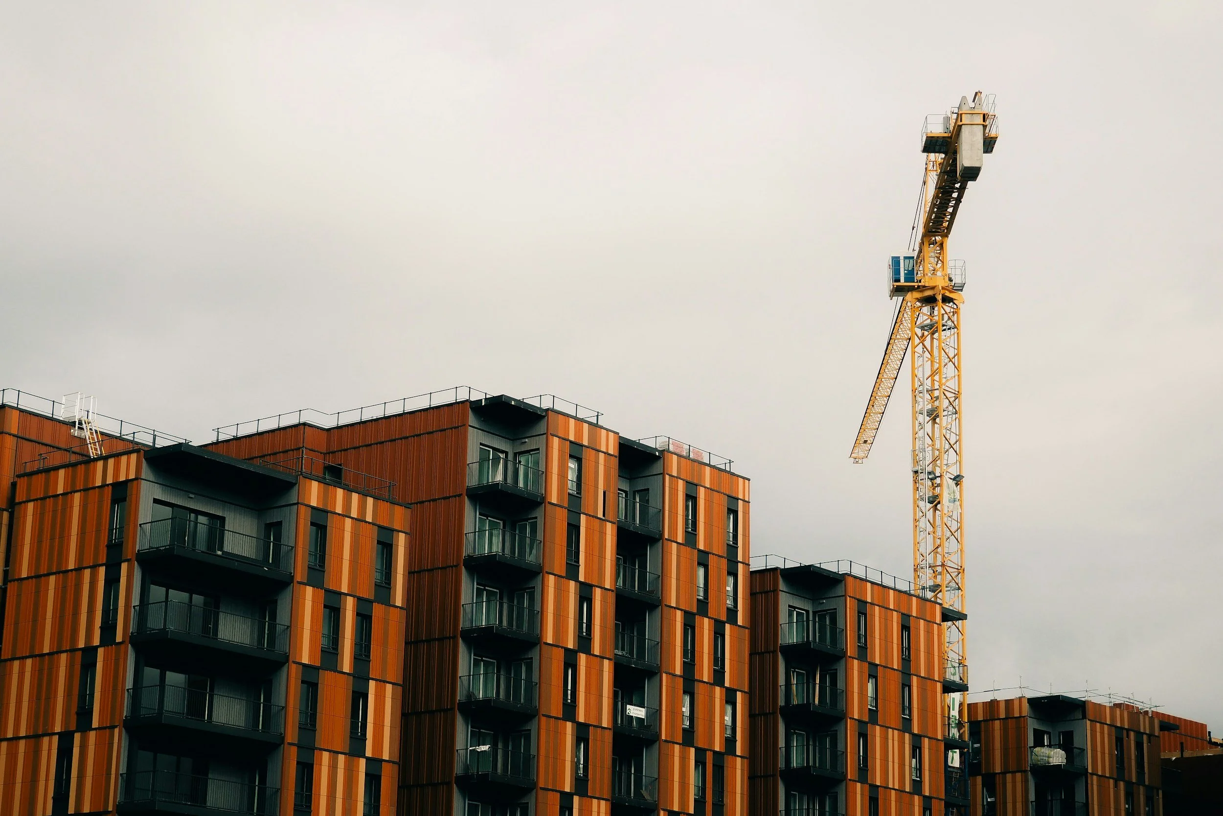 A construction crane next to an orange and gray residential building under an overcast sky.