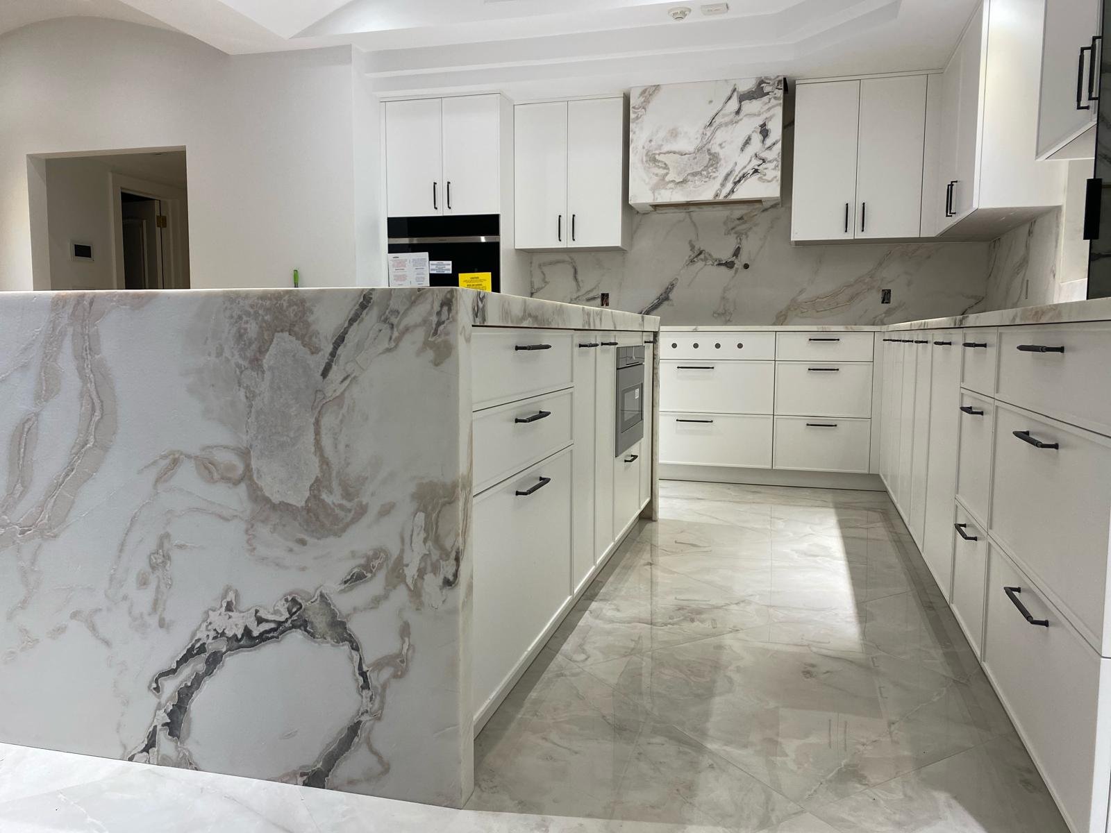 Modern kitchen with white marble countertops and cabinets, black handles, and a built-in oven.