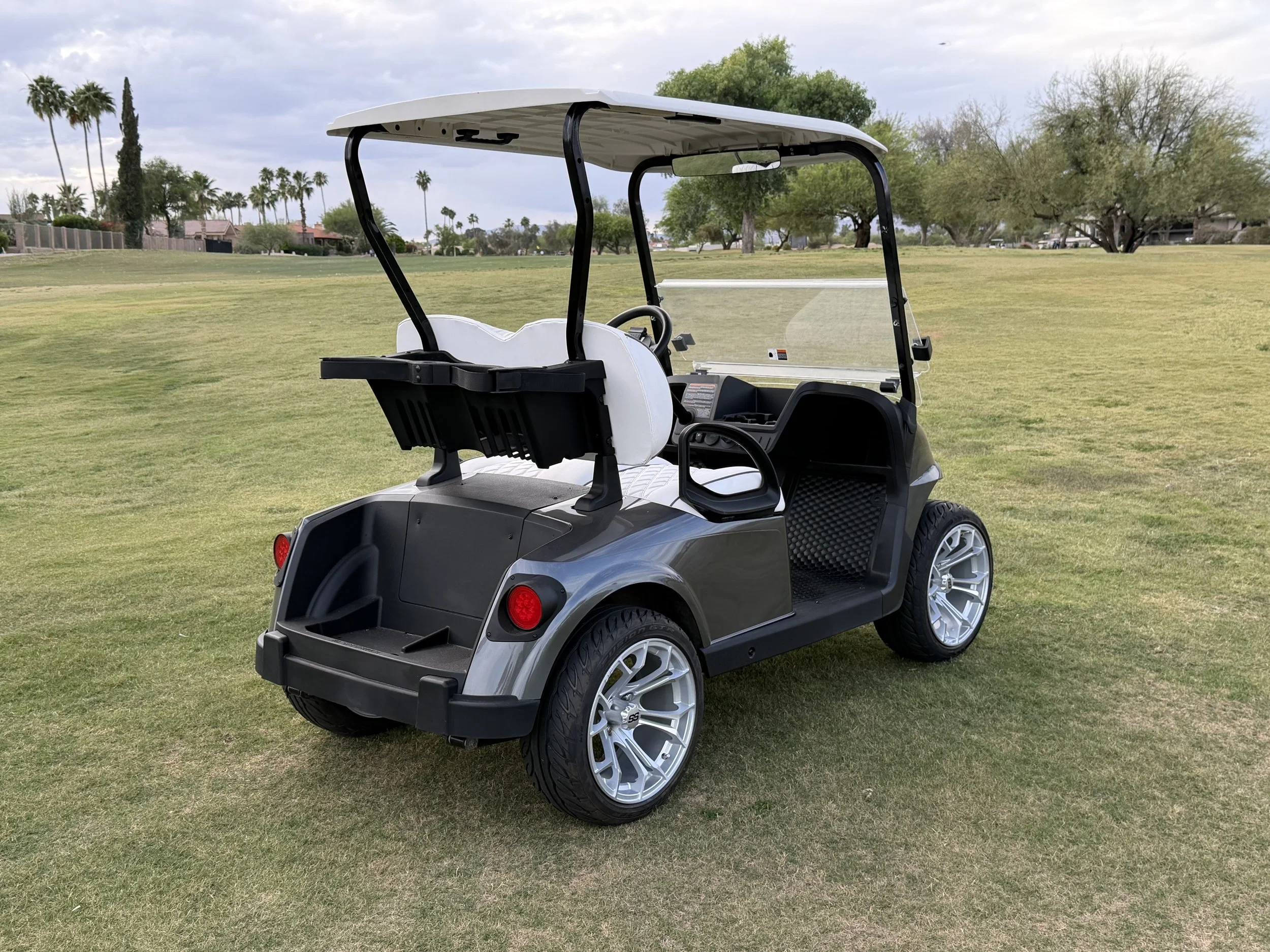 A white and black golf cart parked on a grassy area with trees and cloudy sky in the background. Rio Verde Golf Cart, Fountain Hills, Scottsdale Golf Cart, Scottsdale golf cart repair