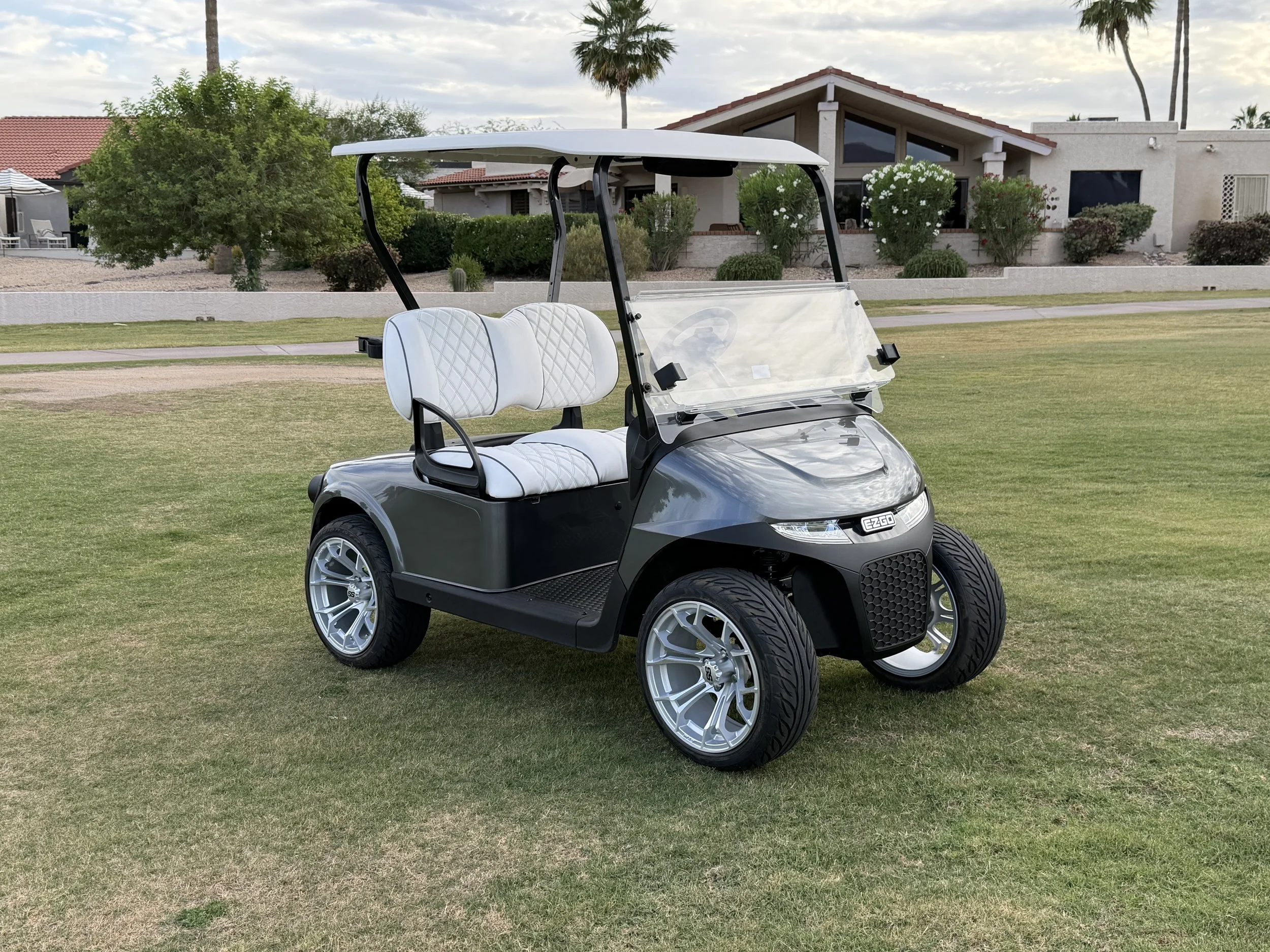 A golf cart parked on a grassy area in front of a house with a desert landscape and palm trees in the background. Rio Verde Golf Cart, Fountain Hills, Scottsdale Golf Cart, Scottsdale golf cart repair