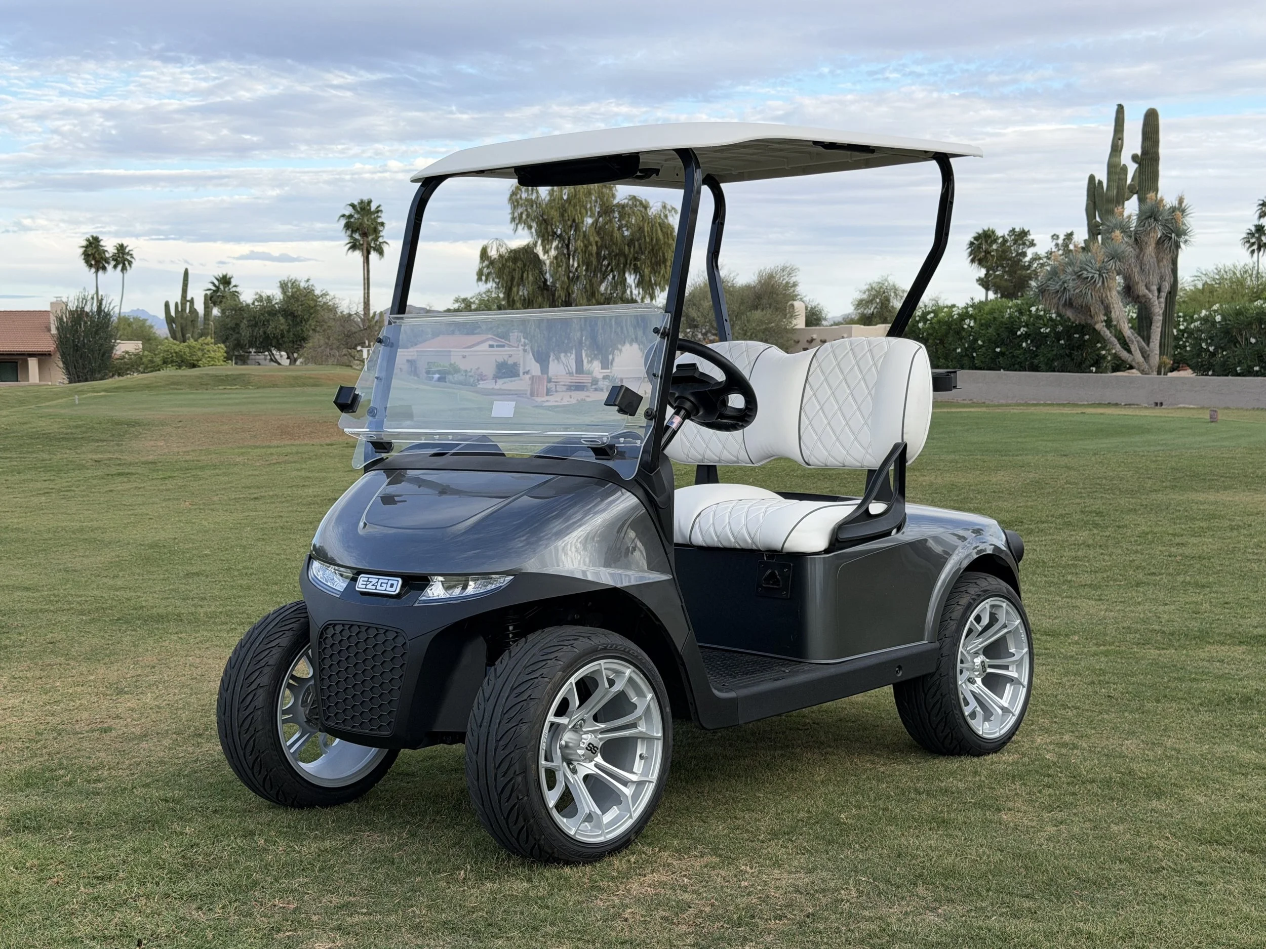 Golf cart on a grassy course with desert trees and cacti, under a partly cloudy sky. Rio Verde Golf Cart, Fountain Hills, Scottsdale Golf Cart, Scottsdale golf cart repair