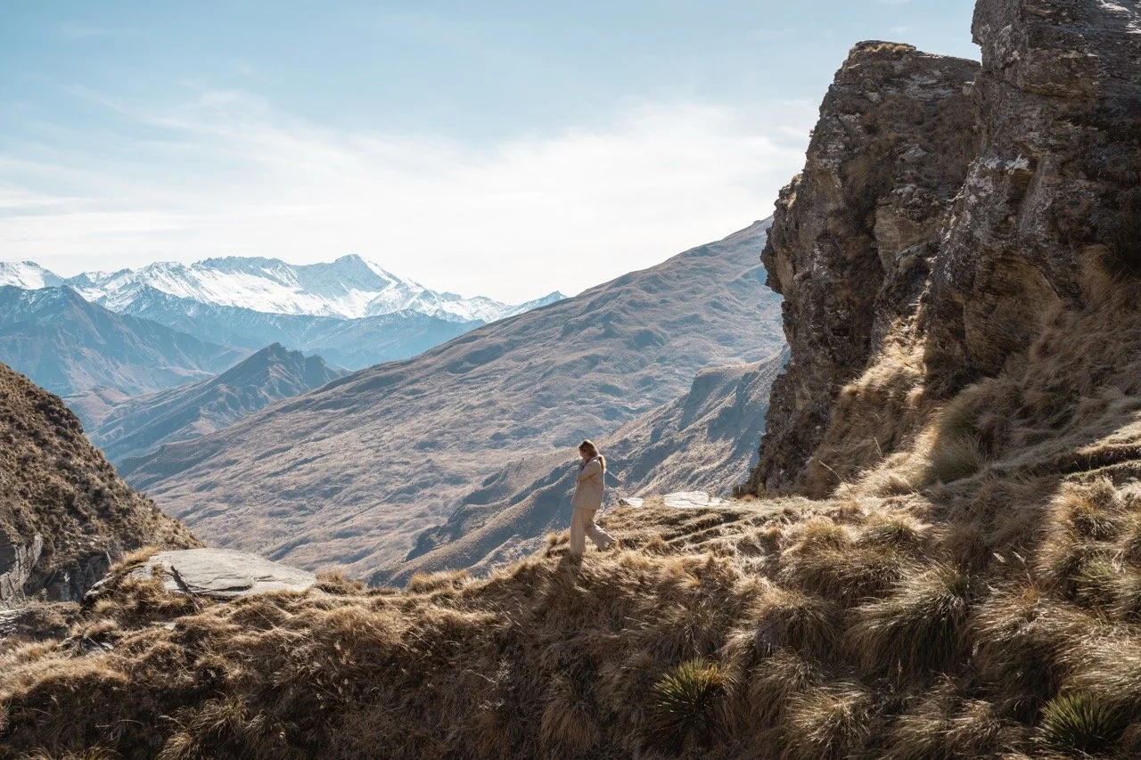 Kelsey walking through the tussocks and hill country with snow capped mountains in the distance.