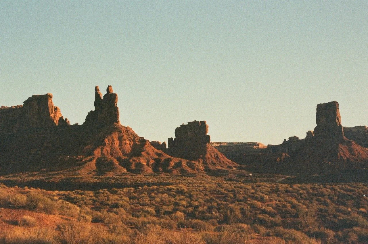 Sunset over a desert landscape with large rock formations and sparse vegetation in the foreground.