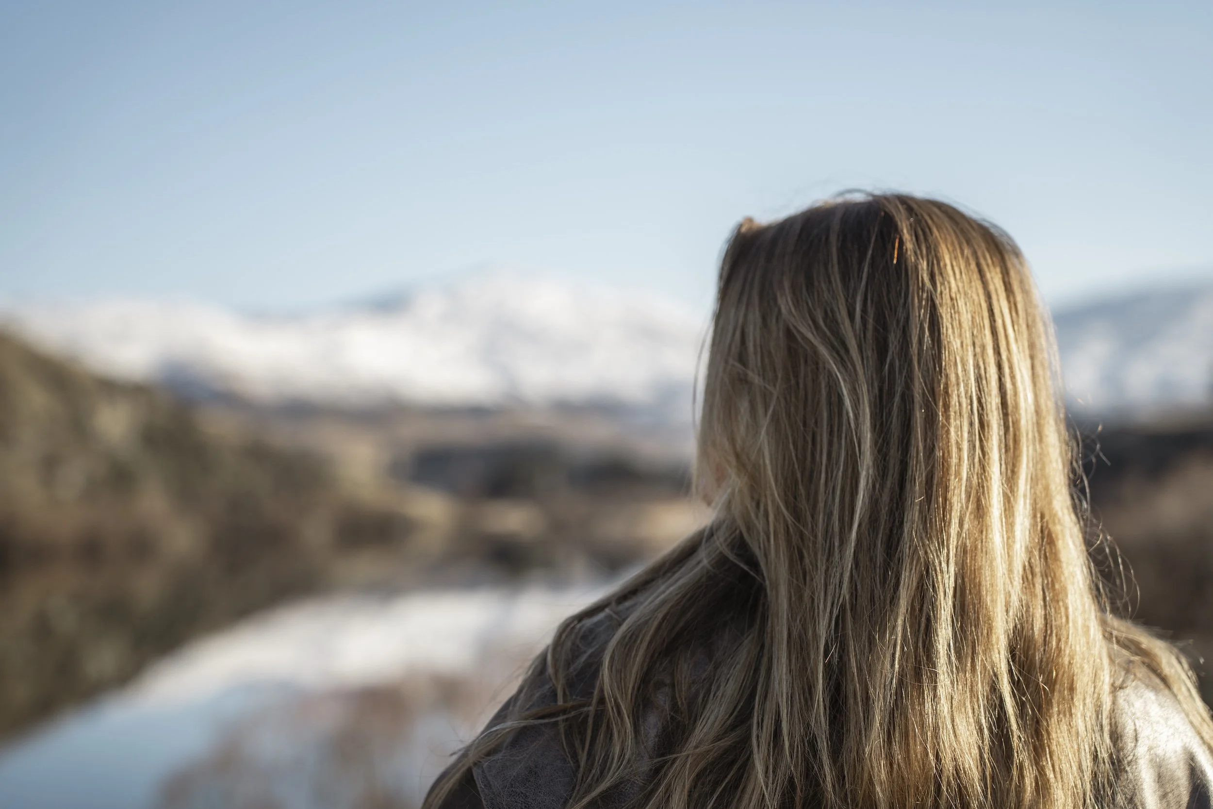 Kelsey standing outdoors in a snowy landscape with mountains in the background under a clear blue sky.