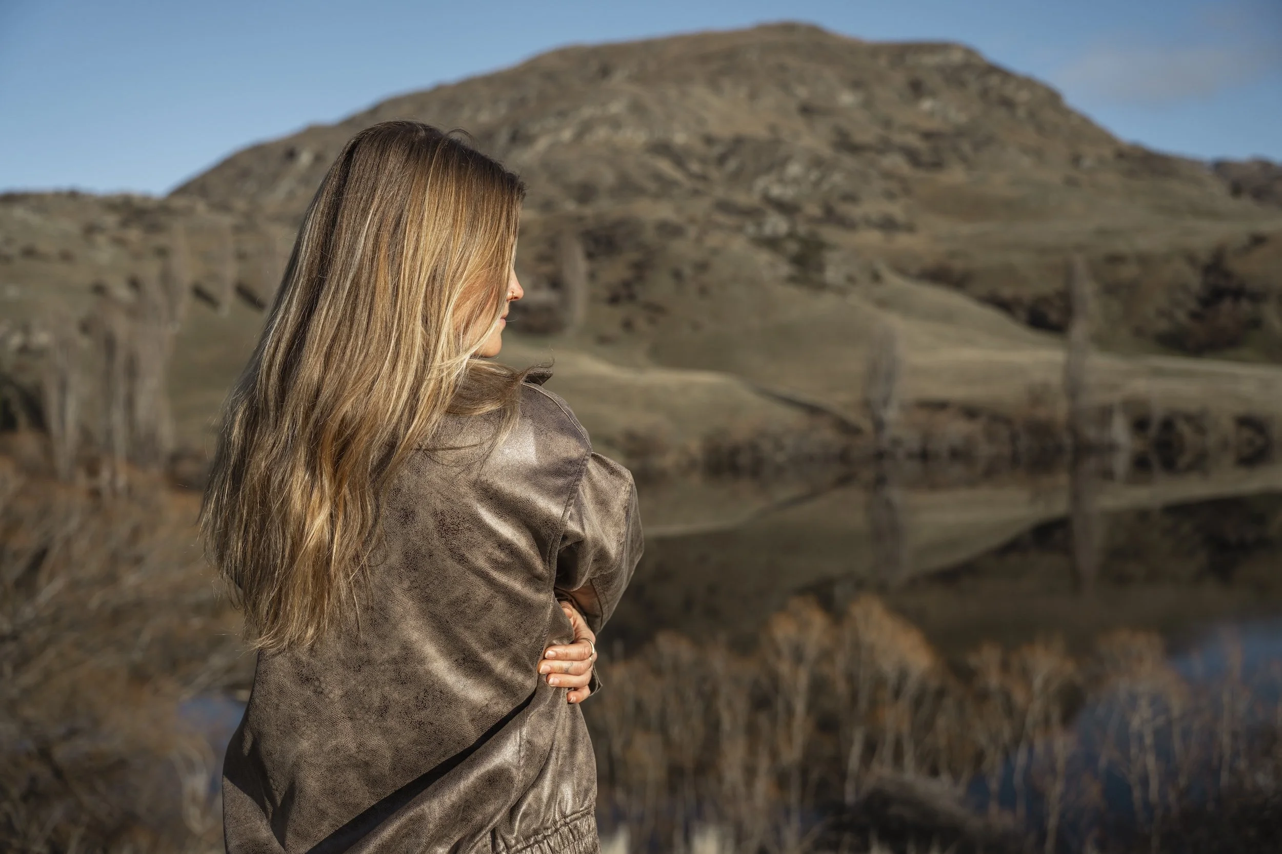Kelsey standing outdoors near Lake Johnson, with rolling hills and a mountain in the background.