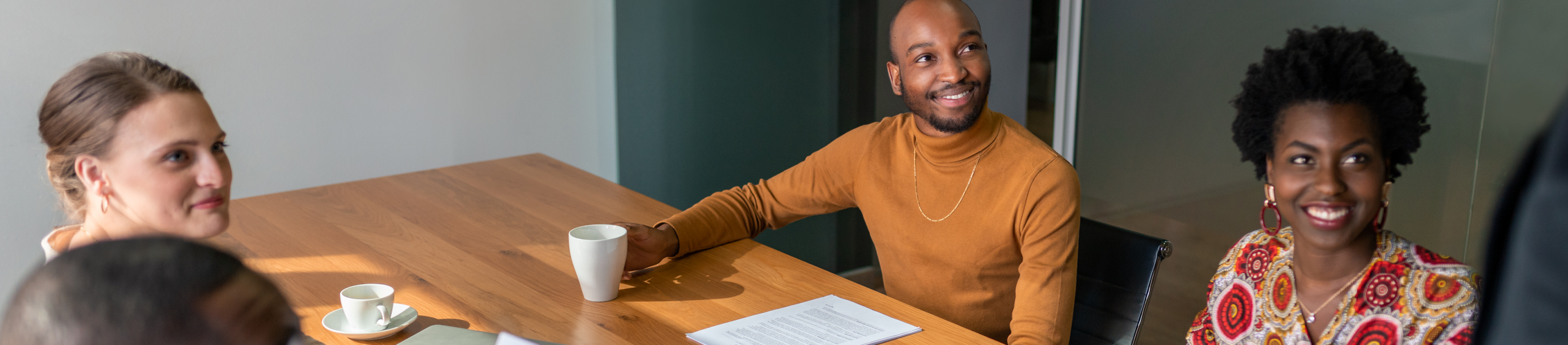 A man in a turtleneck sits at a desk to sign paperwork.