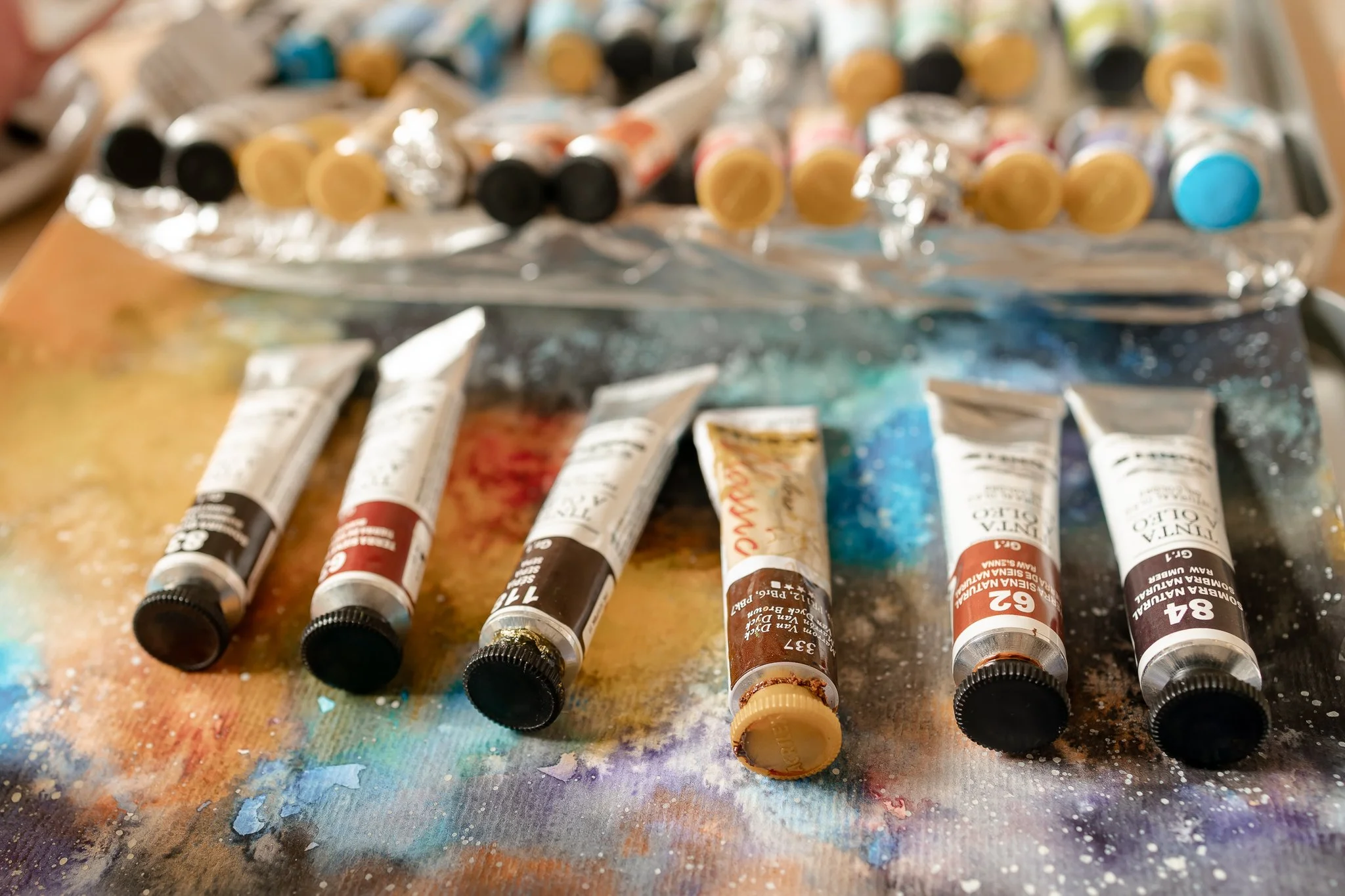Tinta de óleo em tubos variados espalhados sobre uma superfície suja de tinta.