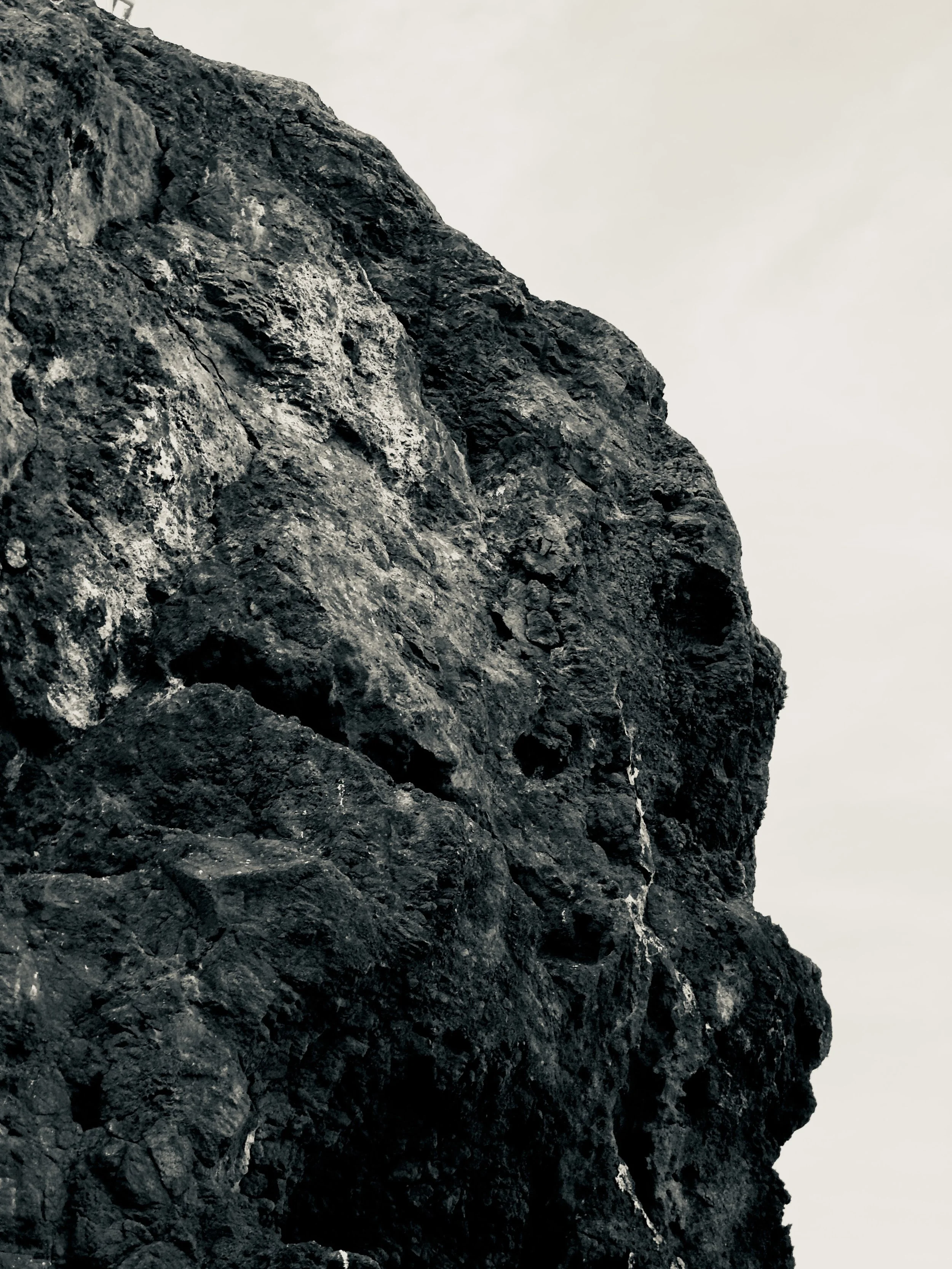 Close-up of a dark, rugged rock formation against a pale, cloudy sky.
